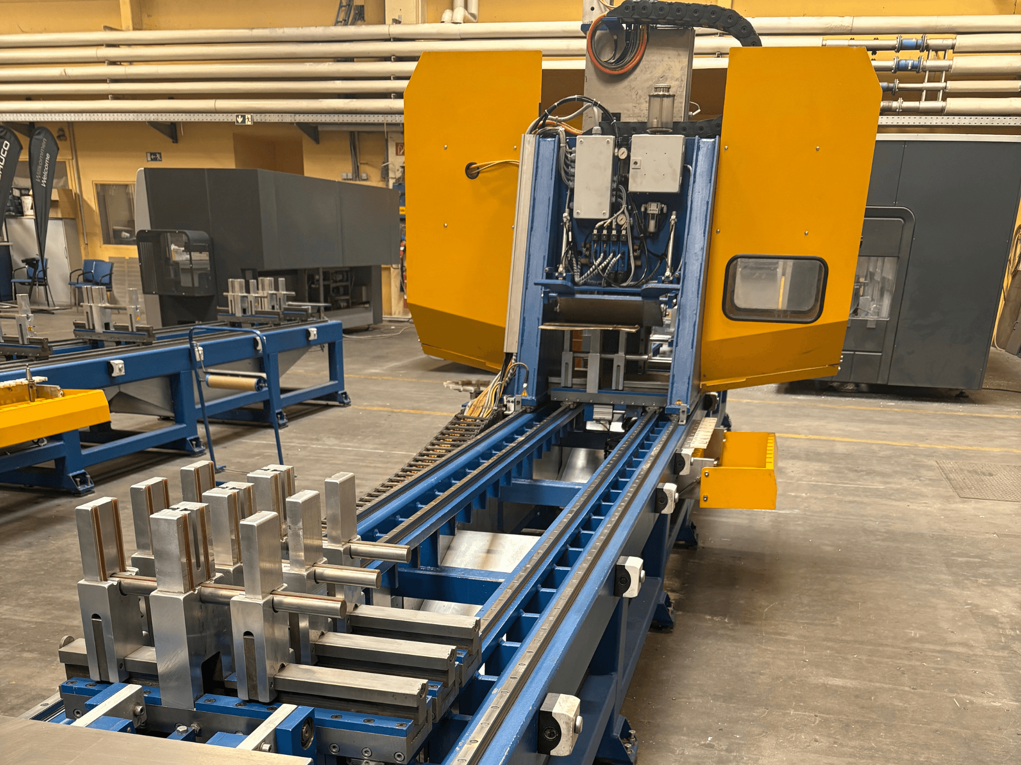 Widok z przodu uniwersalnego centrum obróbczego SCHÜCO PBX AL, prezentującego metalowe elementy na niebieskim łożu obróbczym.