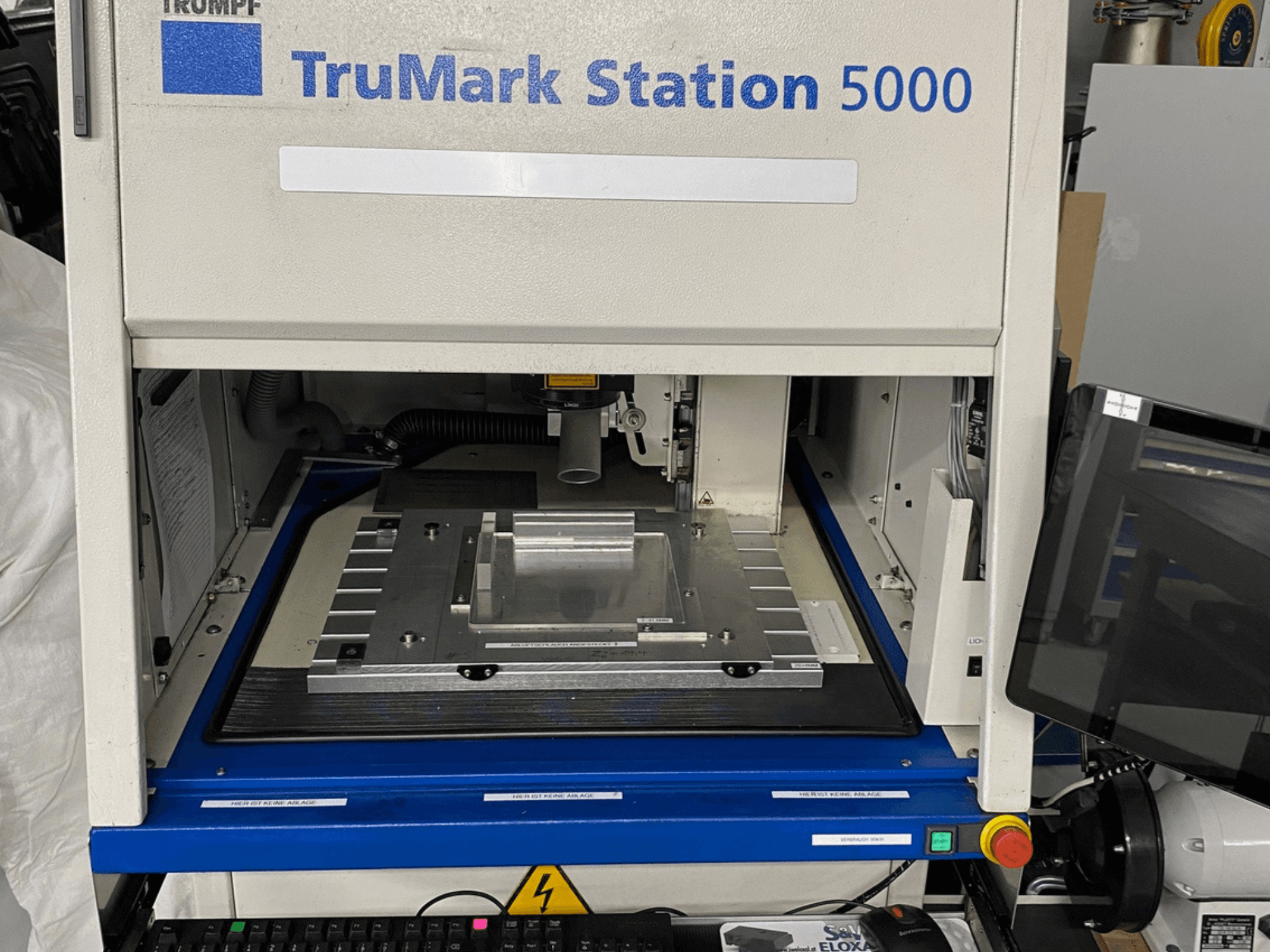 Widok z przodu znakowarki laserowej TruMark Station 5000 przedstawiający stół roboczy, elementy sterujące i ekran monitorowania.