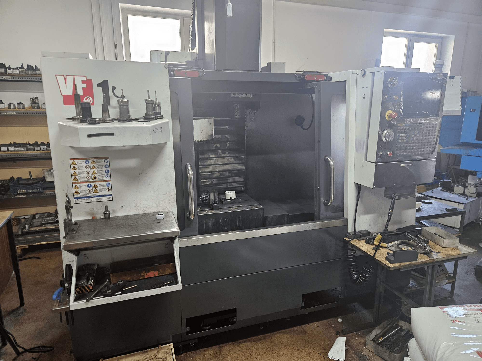 Pionowe centrum obróbcze HAAS VF-1, widok z przodu z narzędziami z boku, widoczny panel sterowania i obszar roboczy w tle.