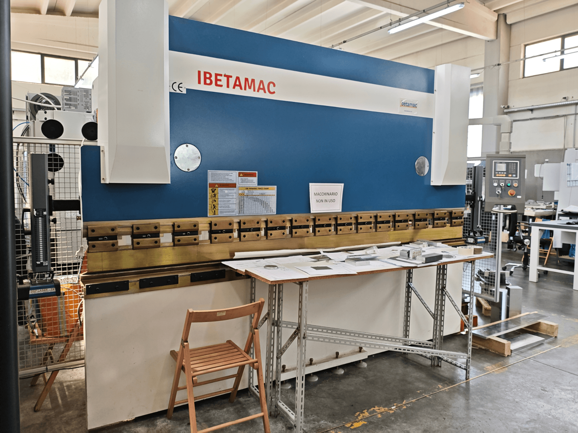 Prasa krawędziowa IBETAMAC 3200 100T w warsztacie – widok z boku przedstawiający panel sterowania, obszar roboczy oraz oznaczenia bezpieczeństwa.