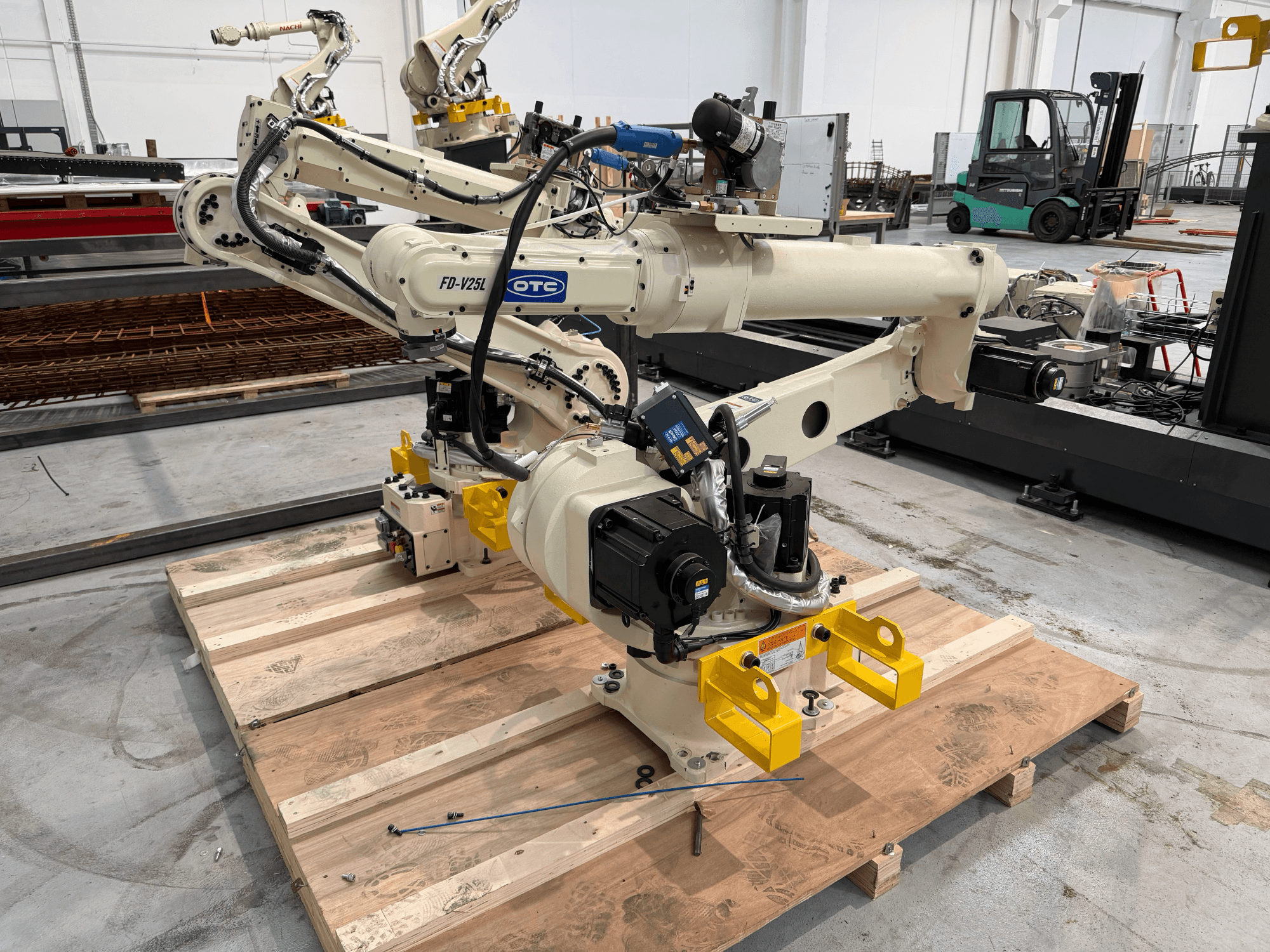 Ramię robota OTC Daihen FD19-V25L widziane z przodu, z żółtymi chwytakami i widocznymi elementami mechanicznymi, umieszczone na drewnianej palecie.