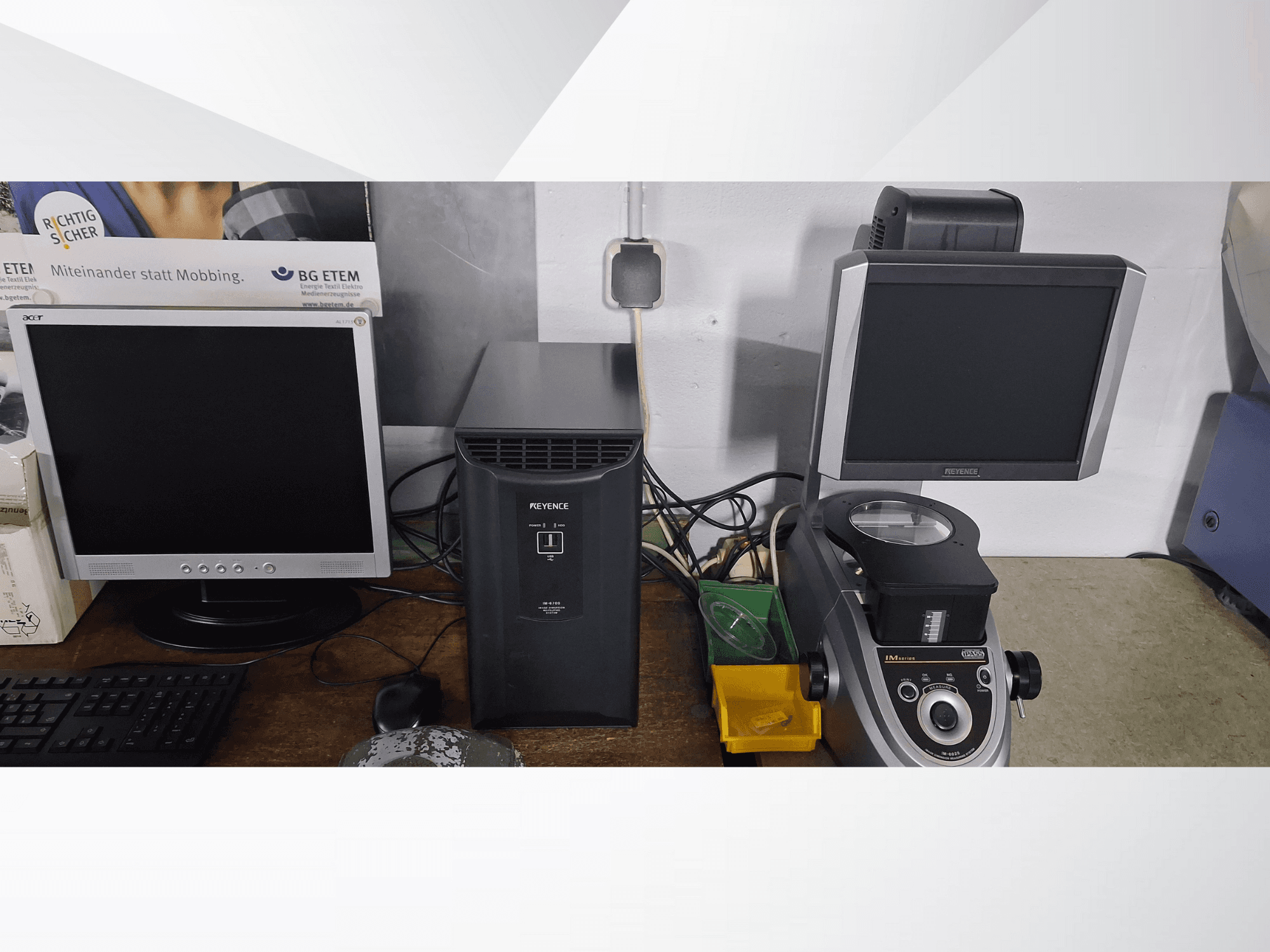 Dwa monitory komputerowe, jeden Acer i jeden Keyence, obok czarnego urządzenia i mikroskopu, patrząc od przodu.
