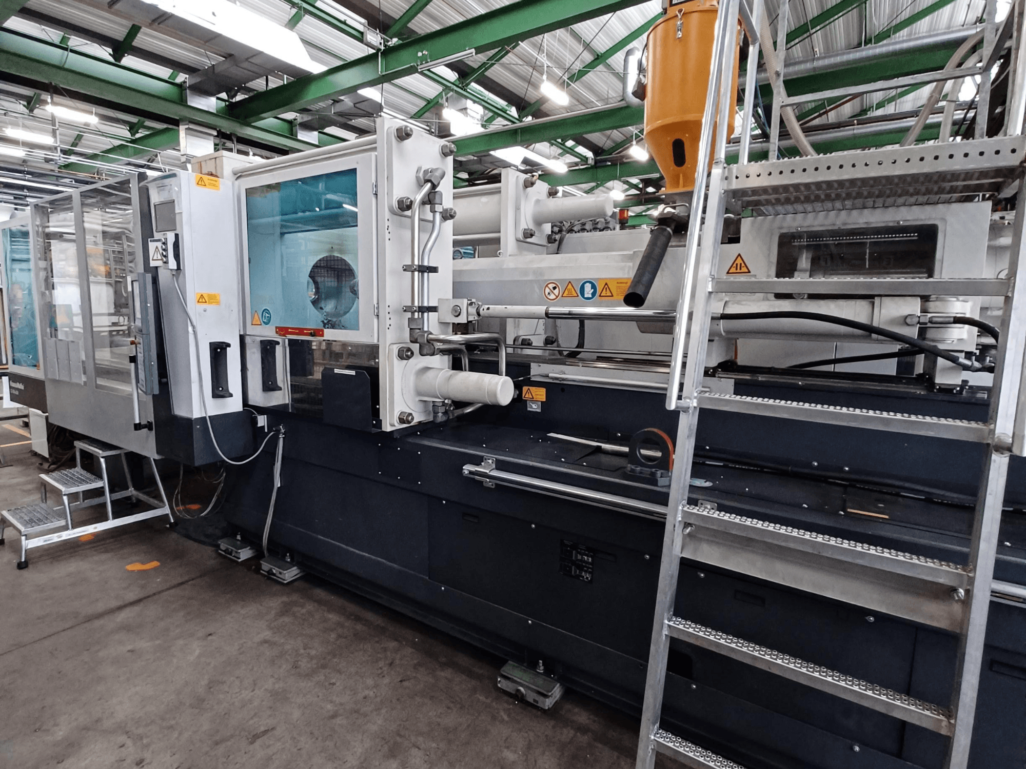 Przemysłowa wtryskarka z wyraźnym widokiem z przodu, pokazująca oznaczenia marki, panel sterowania i zbiornik na materiał.