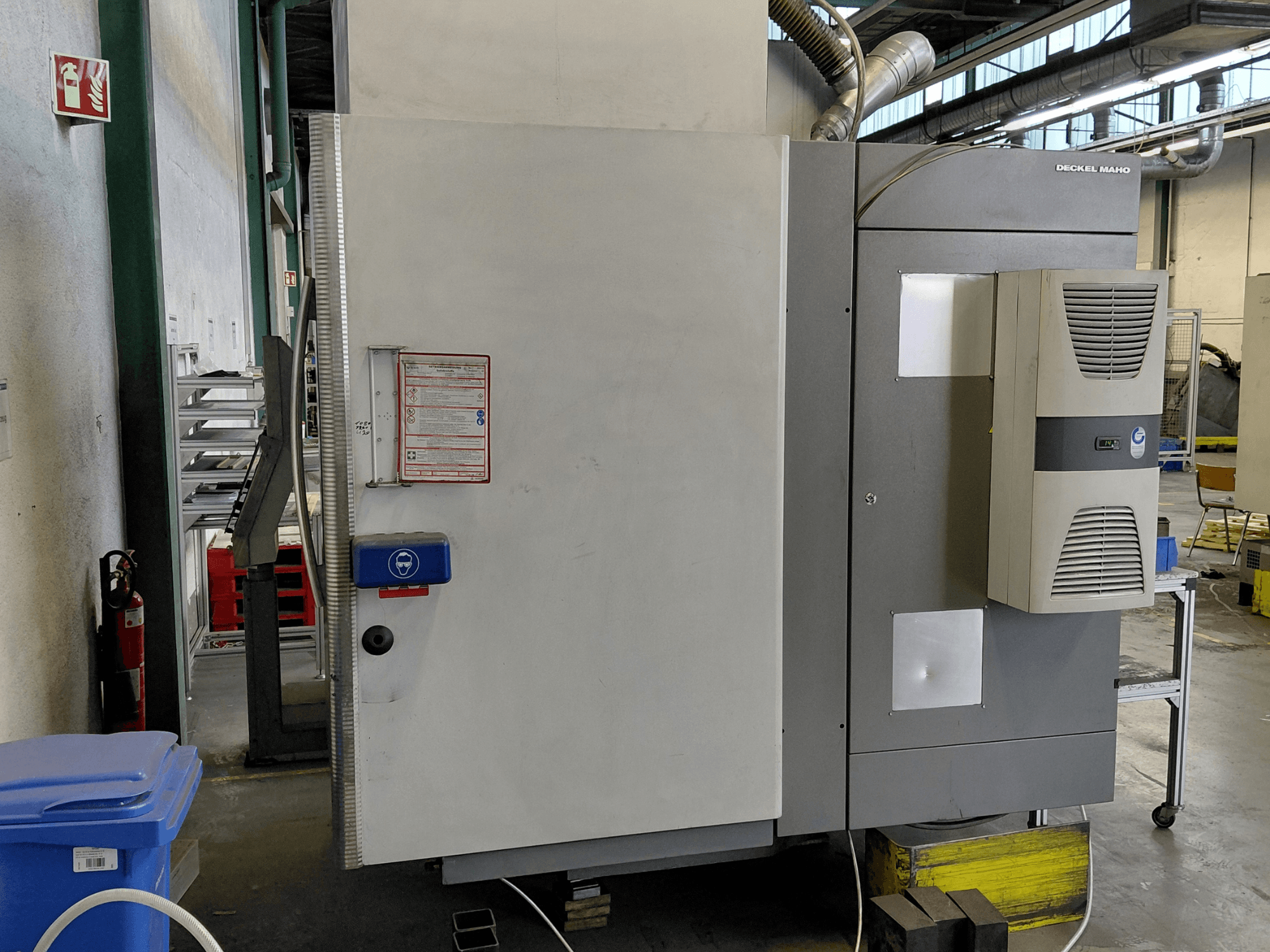 Widok z boku pionowego centrum obróbczego DECKEL MAHO DMC 635 V z widocznym panelem sterowania i etykietami bezpieczeństwa.