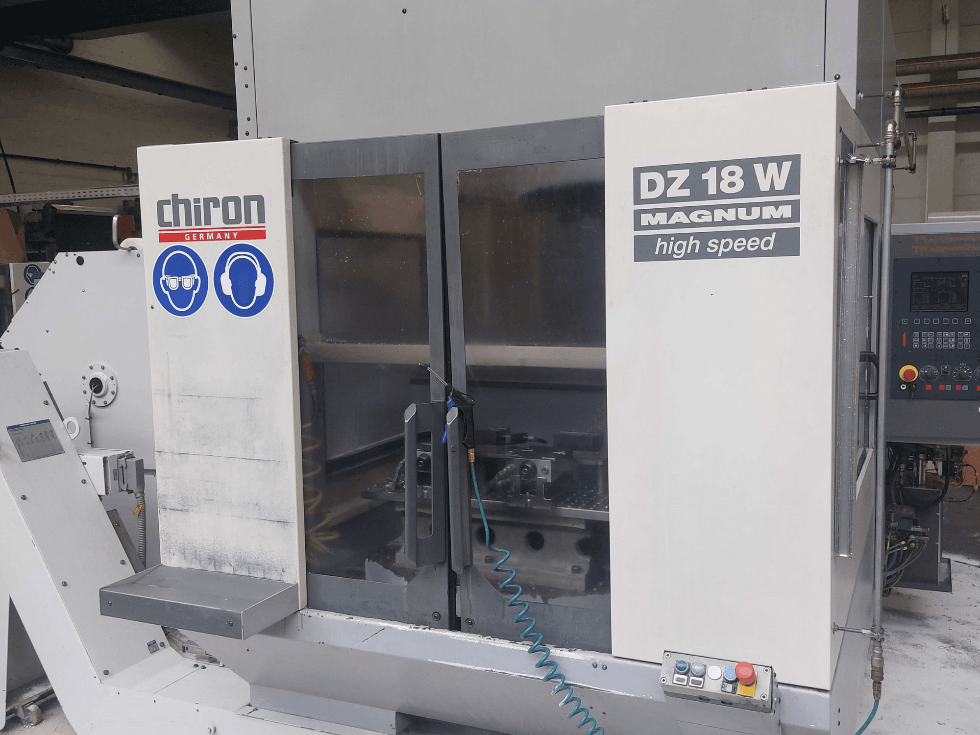 Centrum obróbcze pionowe CHIRON DZ 18 W MAGNUM – widok z przodu przedstawiający panel sterowania i oznaczenia bezpieczeństwa.