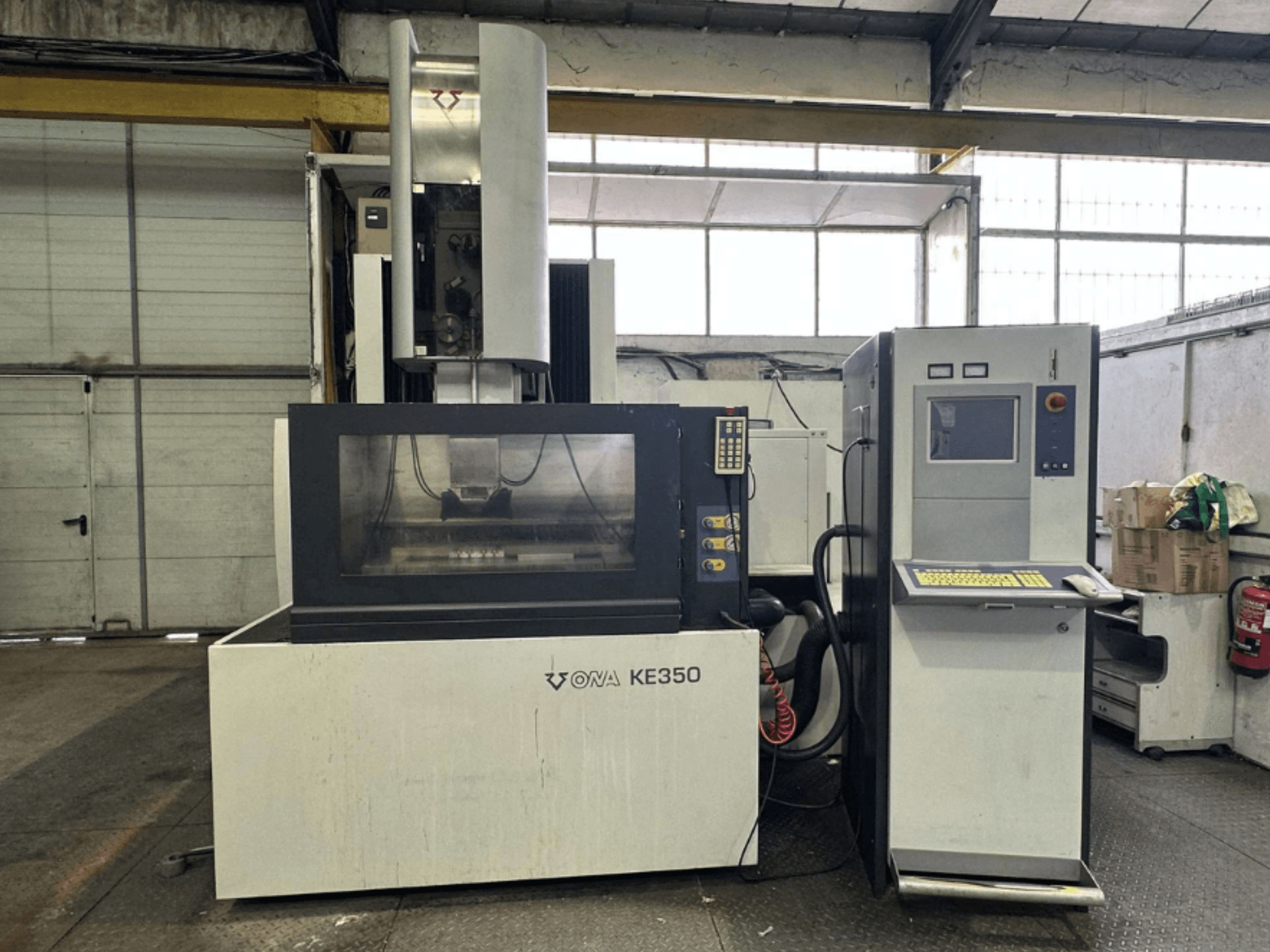Widok z przodu maszyny CNC ONA KE350 z panelem sterowania, ekranem i różnymi przyciskami, znajdującej się w środowisku przemysłowym.