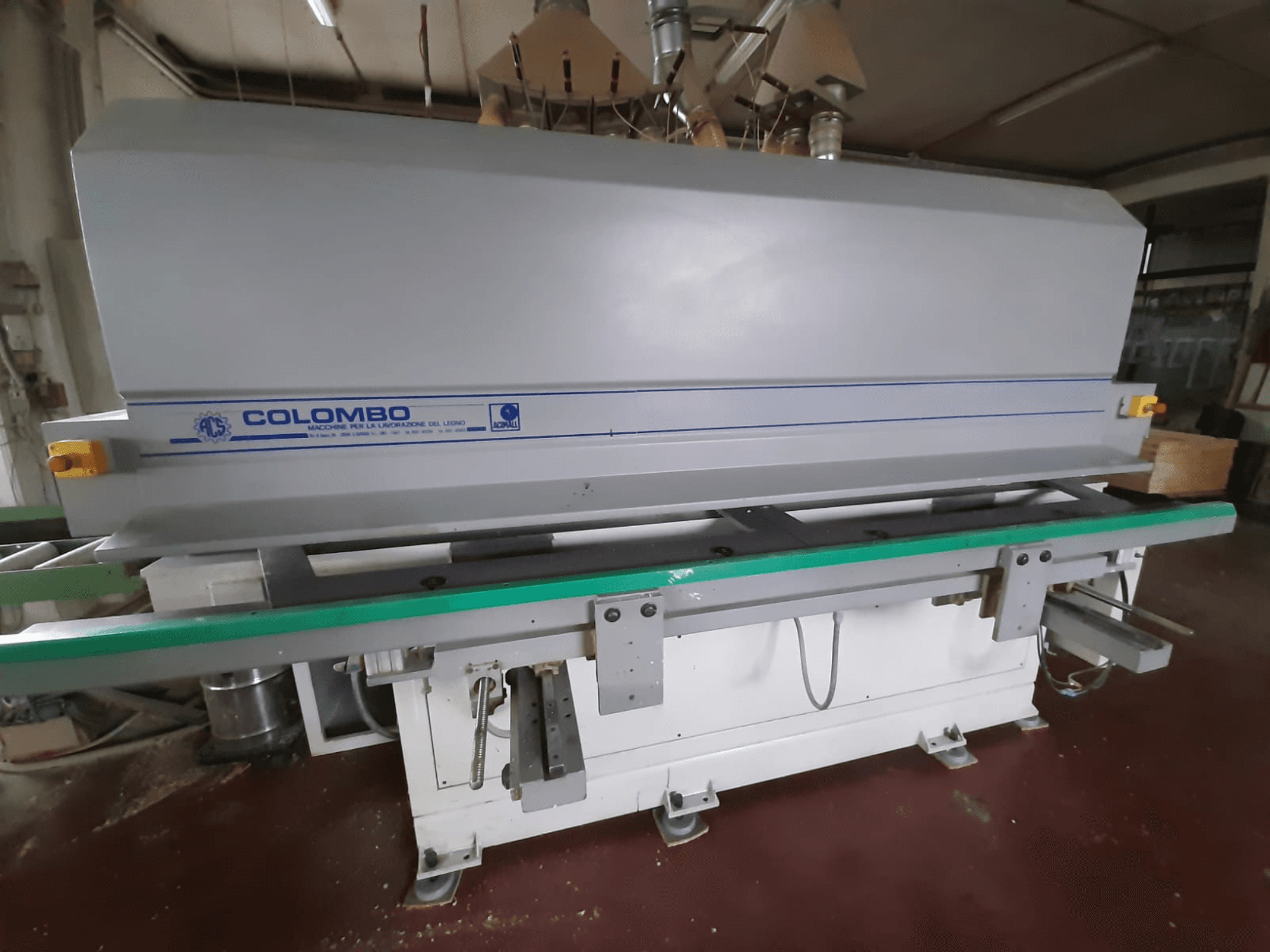 Maszyna do obróbki drewna Colombo, widok z przodu, z długim zielonym stołem, przyciskami sterującymi i szarym korpusem z niebieskimi akcentami.