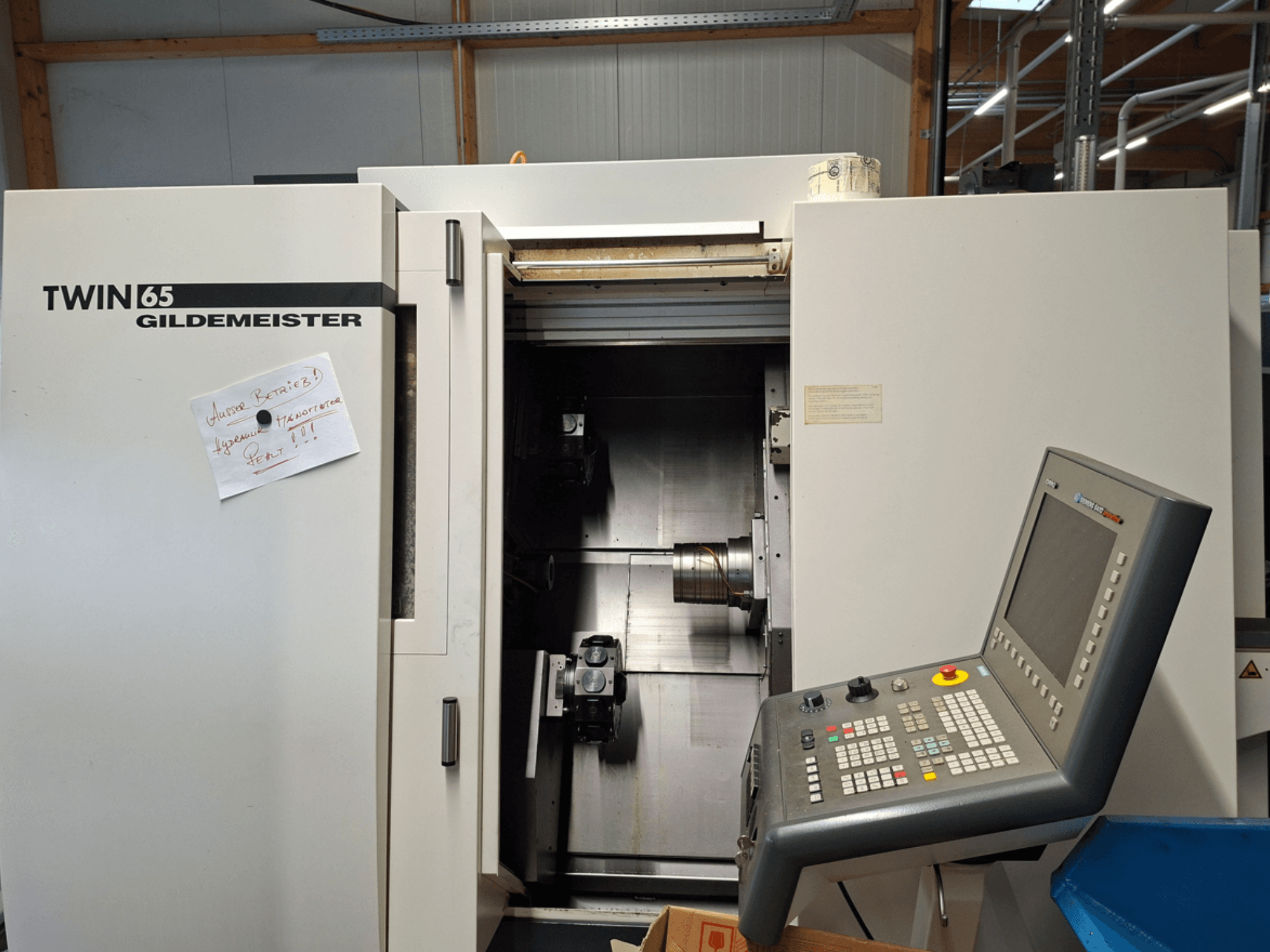 Tokarka CNC Gildemeister TWIN 65, widok z przodu przedstawiający panel sterowania i częściowo otwartą komorę z widocznymi maszynami.