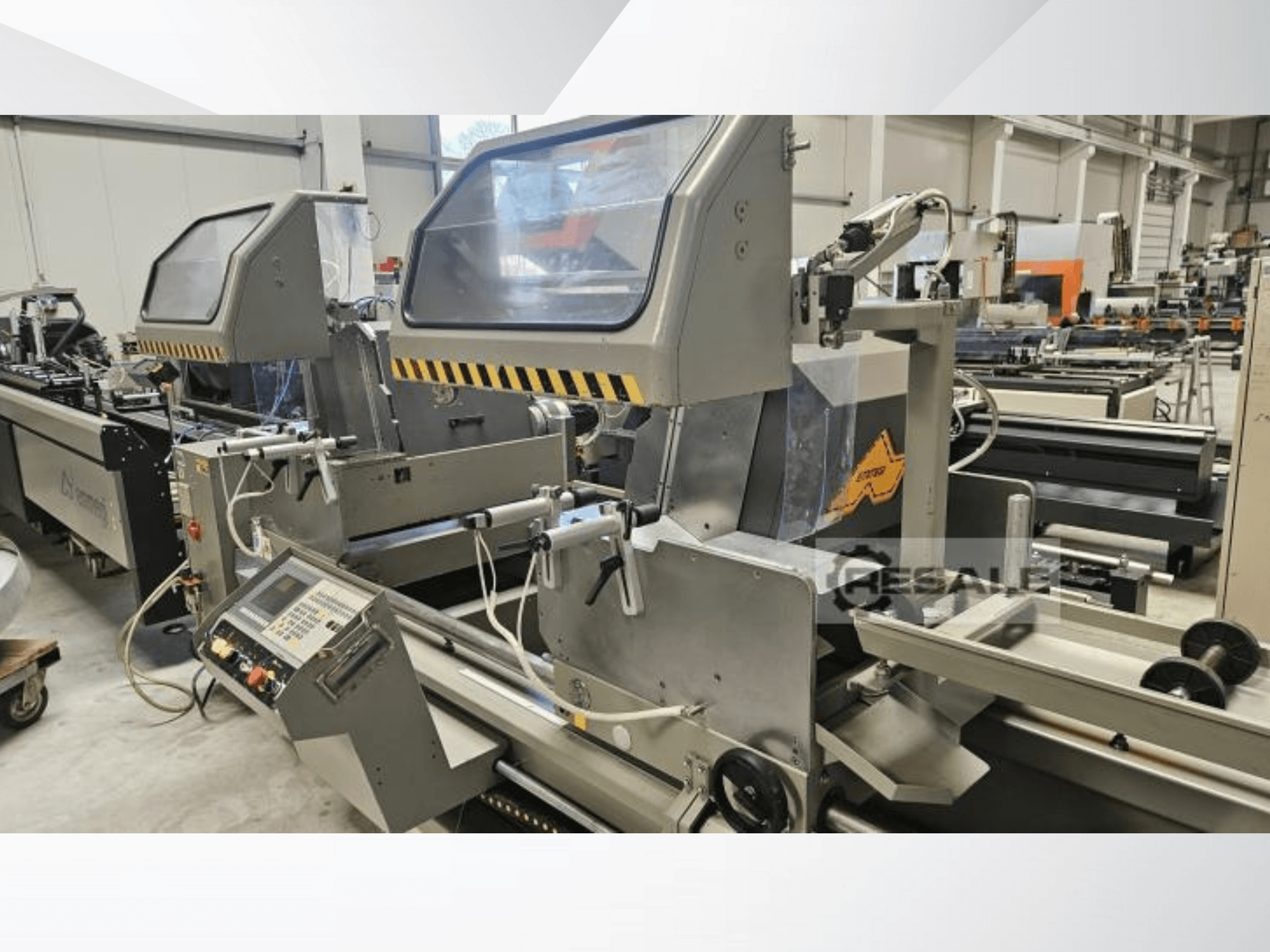 Podwójna pilarka w warunkach fabrycznych; widok z przodu przedstawiający panel sterowania, szklane osłony i elementy tnące.