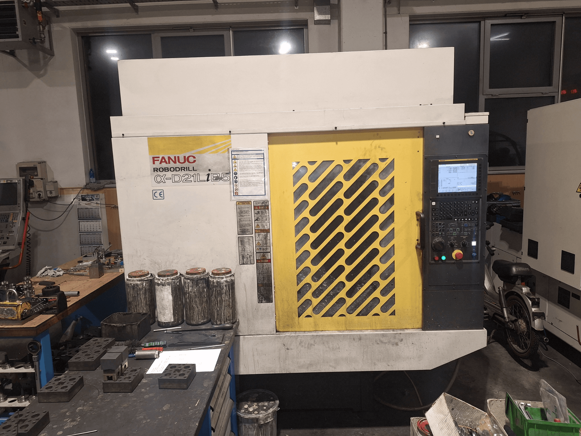 Widok z przodu FANUC Robodrill α-D21LiB5, pokazujący panel sterowania, żółtą kratkę i pobliskie narzędzia na stole warsztatowym.
