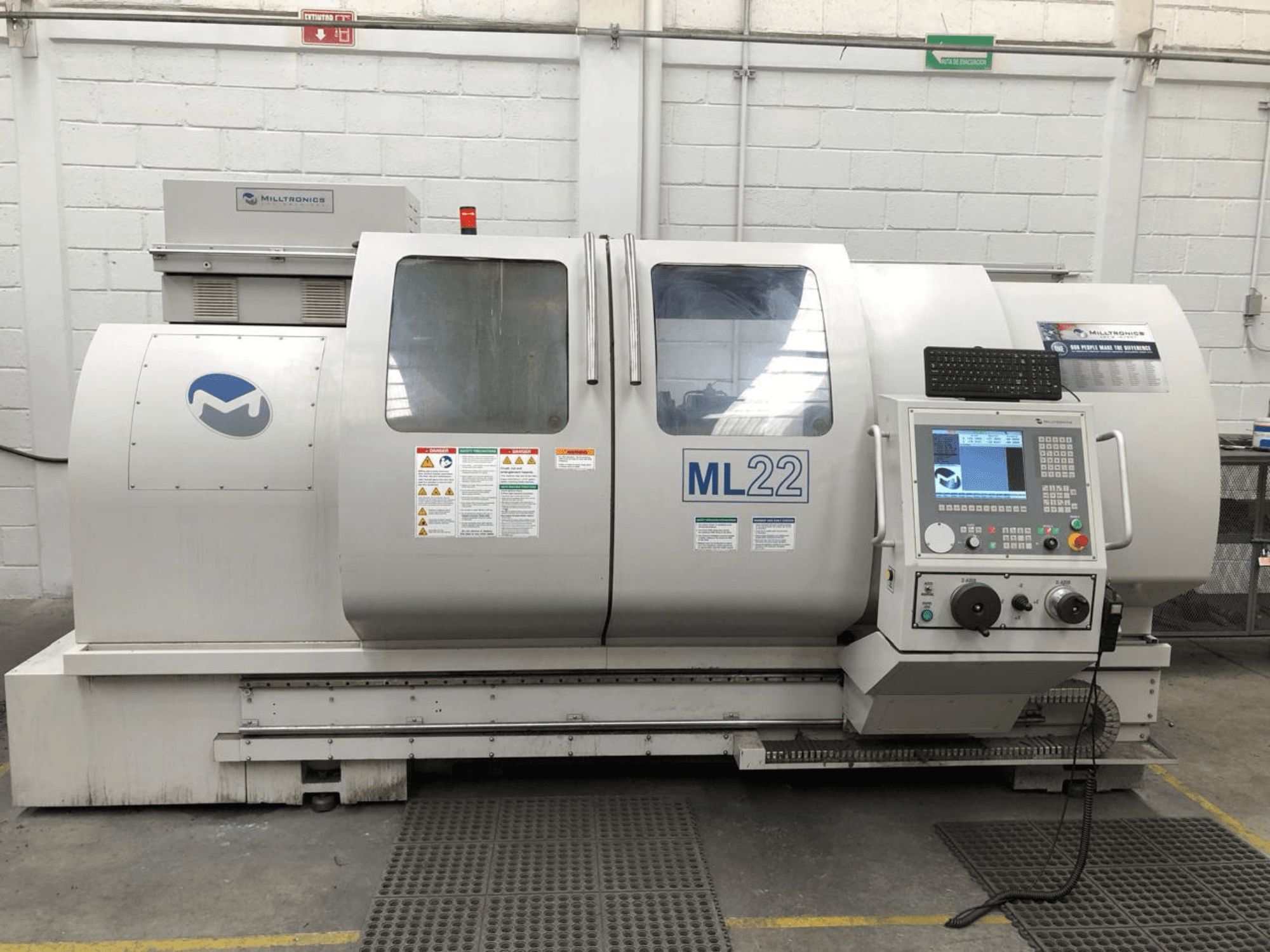 Pionowe centrum obróbcze MILLTRONICS RH 20, widok z przodu przedstawiający panel sterowania, logo marki i etykiety bezpieczeństwa na maszynie.