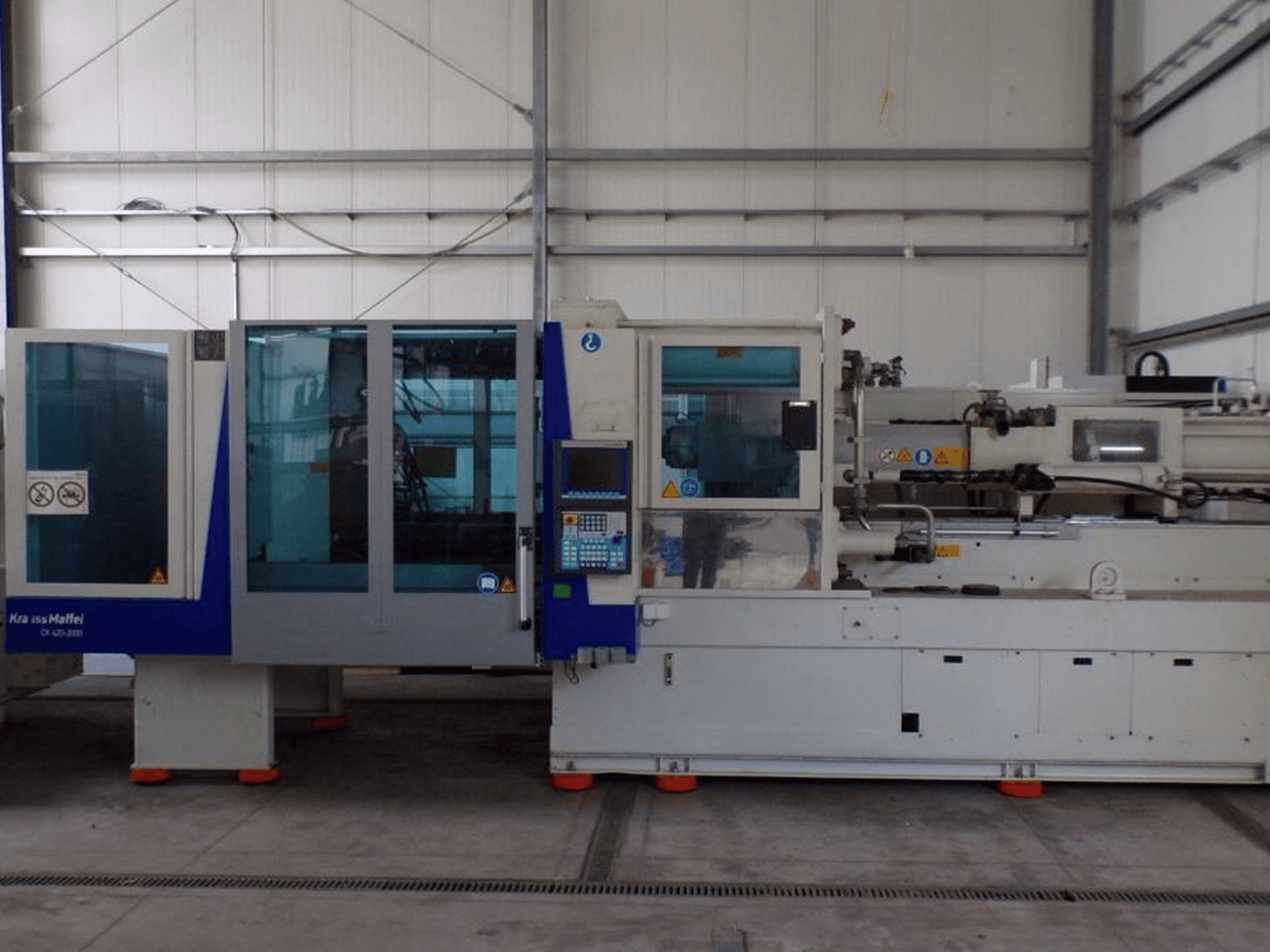Wtryskarka KraussMaffei, widok z boku, z panelem sterowania i wskaźnikami bezpieczeństwa, widoczna w warunkach fabrycznych.