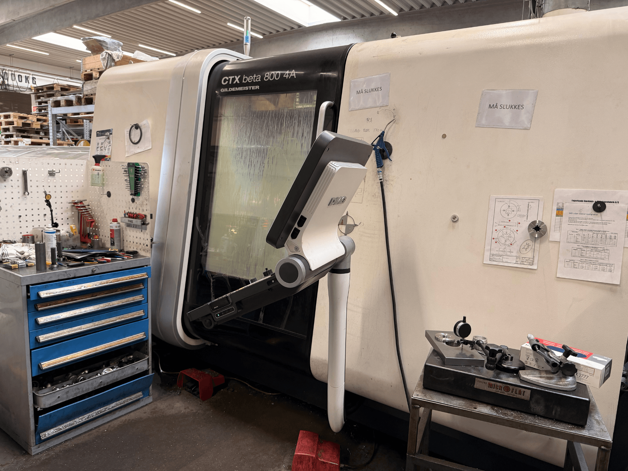 Tokarka pionowa DMG MORI CTX Beta 800 4a w warsztacie, z ramieniem sterującym i dokumentacją techniczną w pobliżu.