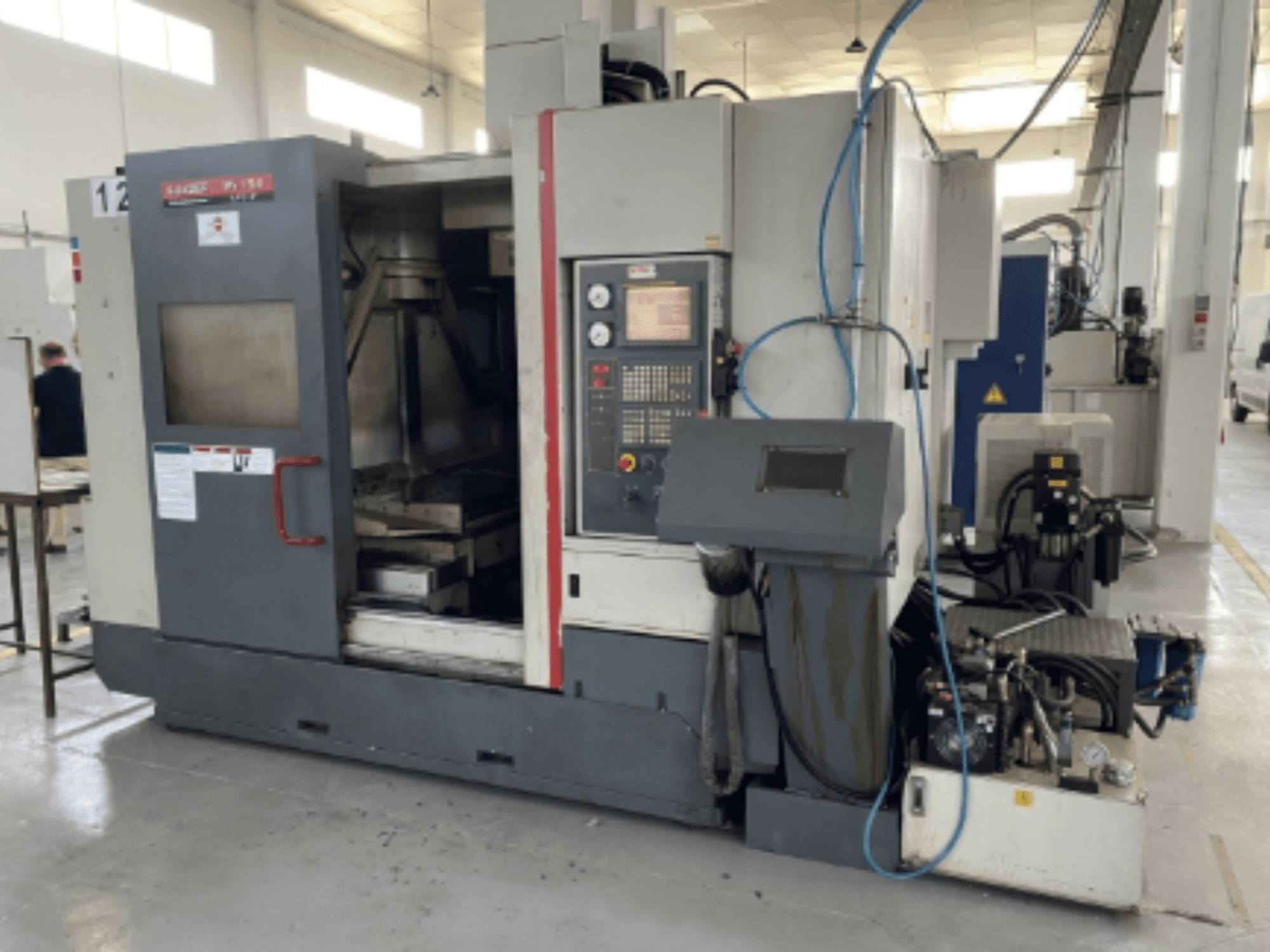 Pionowe centrum obróbcze Quaser MV154APC-912, widok z przodu przedstawiający panel sterowania, otwarte drzwi i komponenty maszyny.