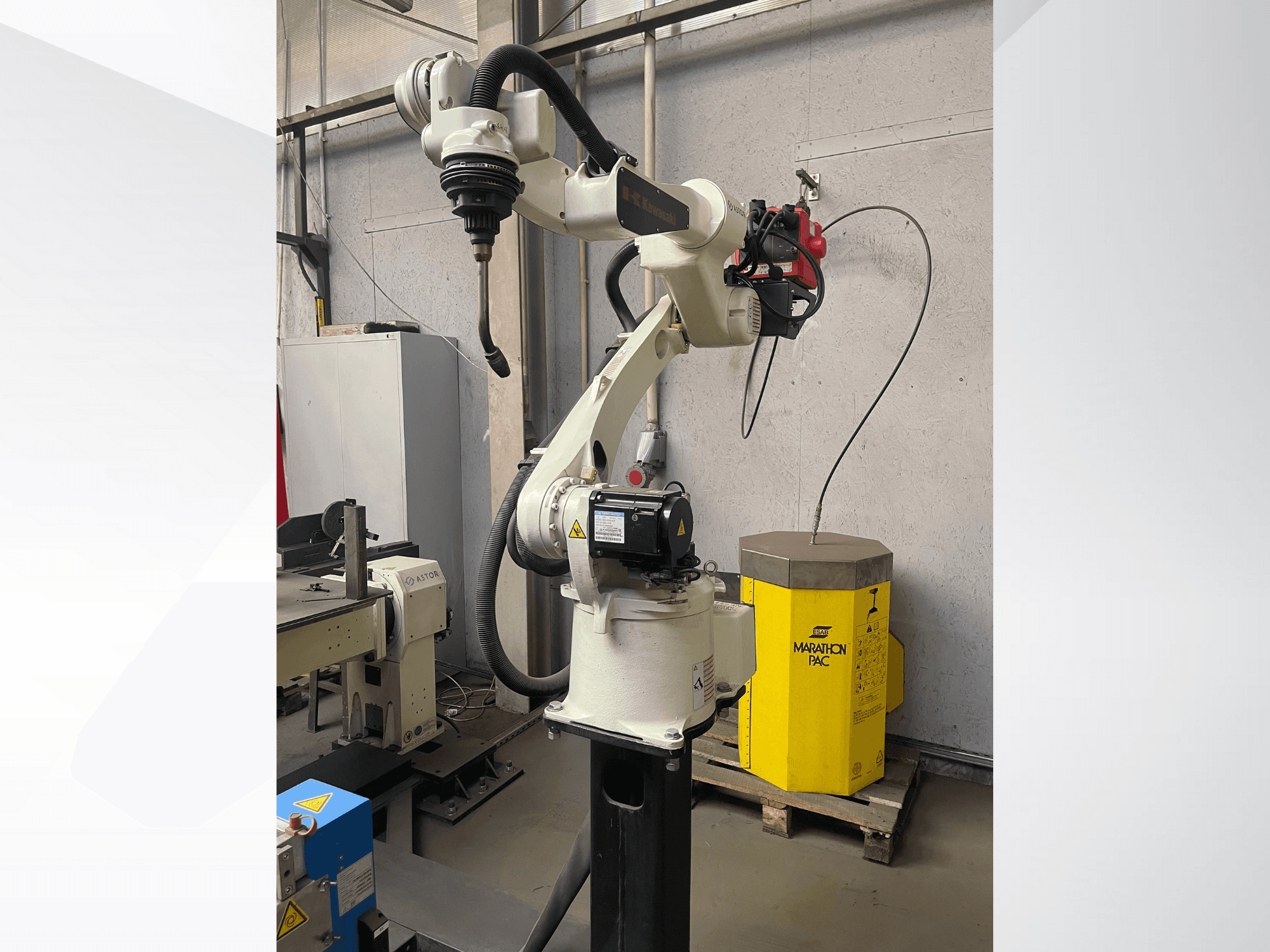 Ramię robota Kawasaki w widoku z boku, z zamontowanym uchwytem na narzędzia, z żółtą jednostką zasilającą w tle.