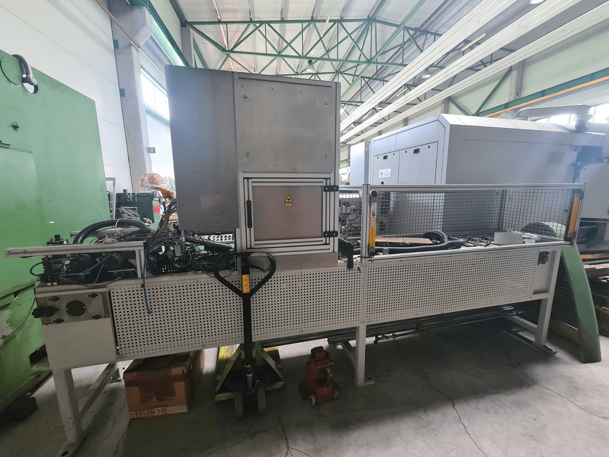 Maszyna przemysłowa z metalową ramą, wężami i panelem sterowania, widziana z boku w fabryce.
