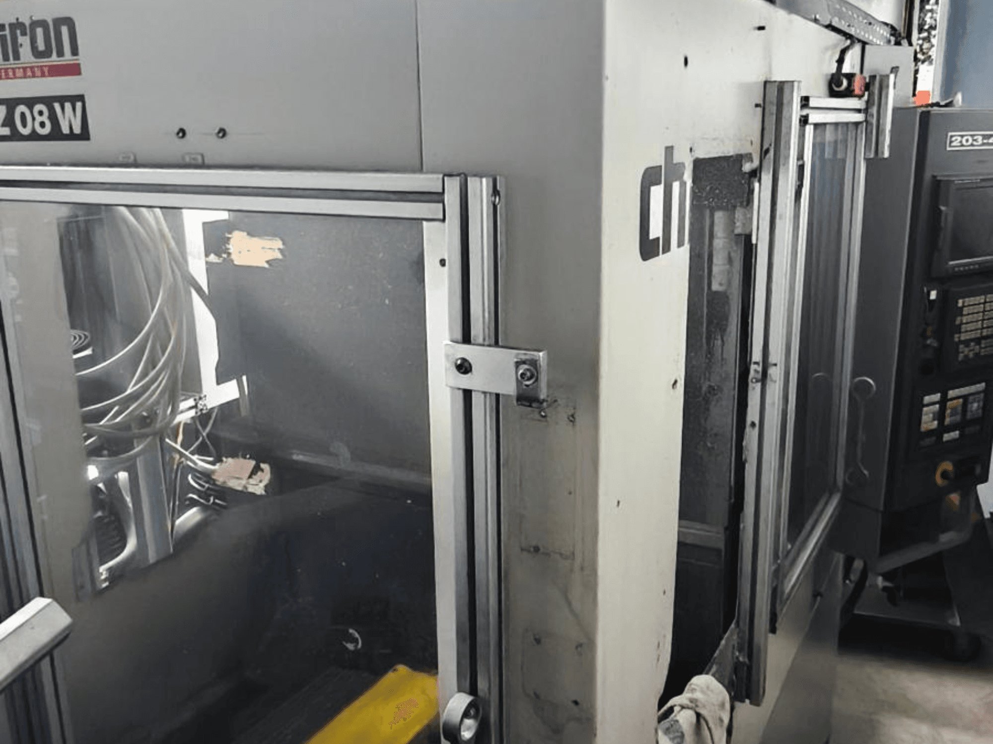 Pionowe centrum obróbcze CHIRON FZ 08 W, widok z przodu przedstawiający panel sterowania i częściowo otwarte drzwi, z widocznymi elementami wewnętrznymi.