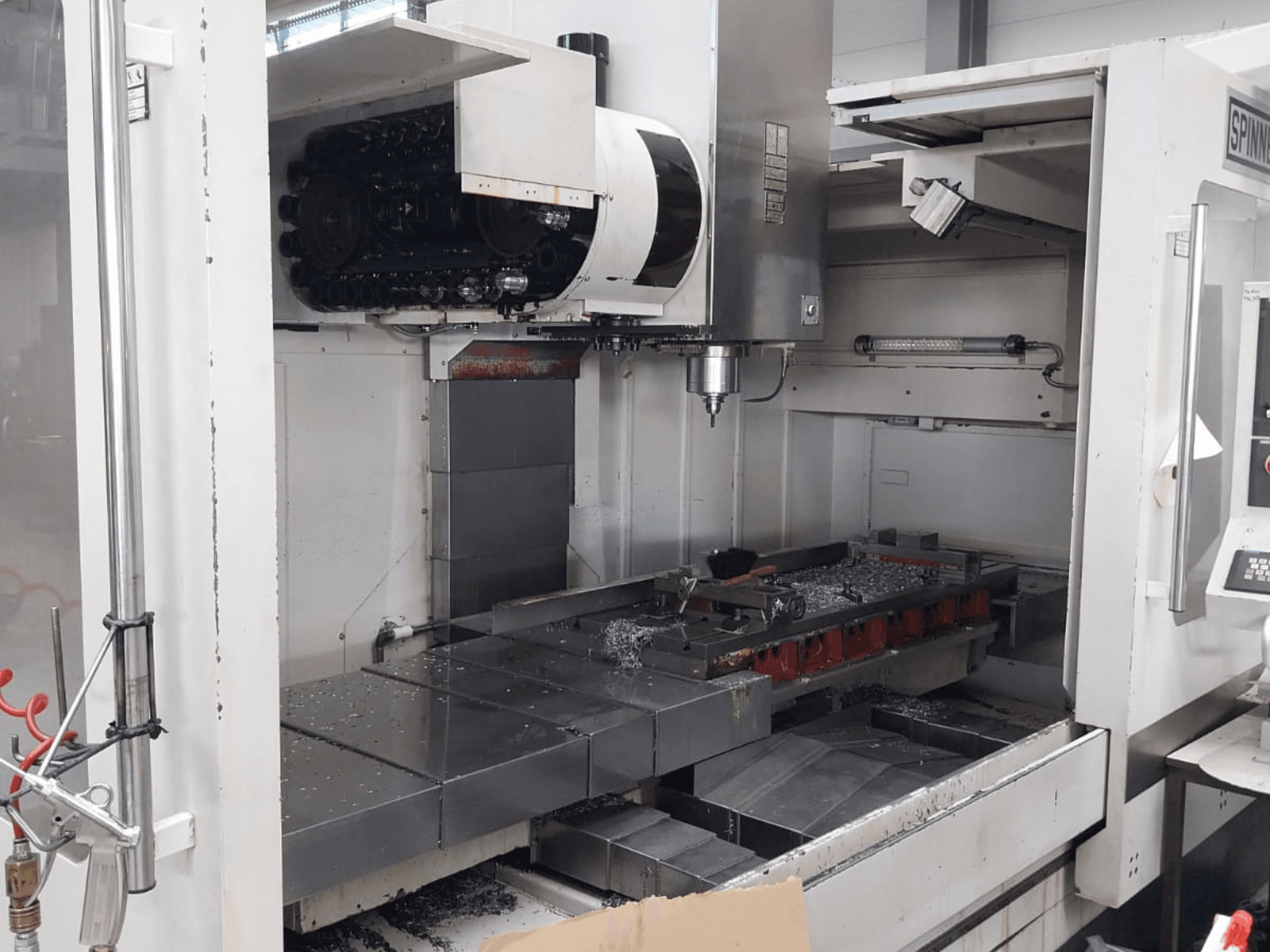 Widok z przodu pionowego centrum obróbczego SPINNER MVC 1600 przedstawiający otwartą przestrzeń roboczą, wrzeciono i metalowe wióry na stole.
