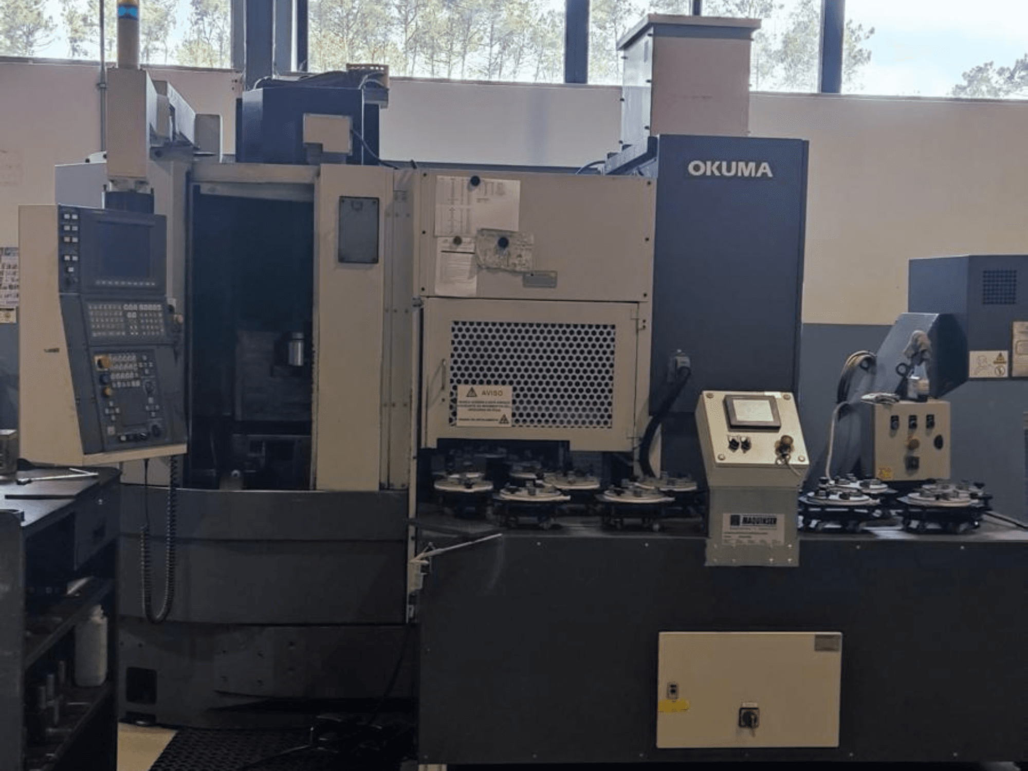 Pionowa tokarka Okuma LVT300 w widoku z przodu, z panelem sterowania, uchwytami narzędzi i obszarem obróbki.