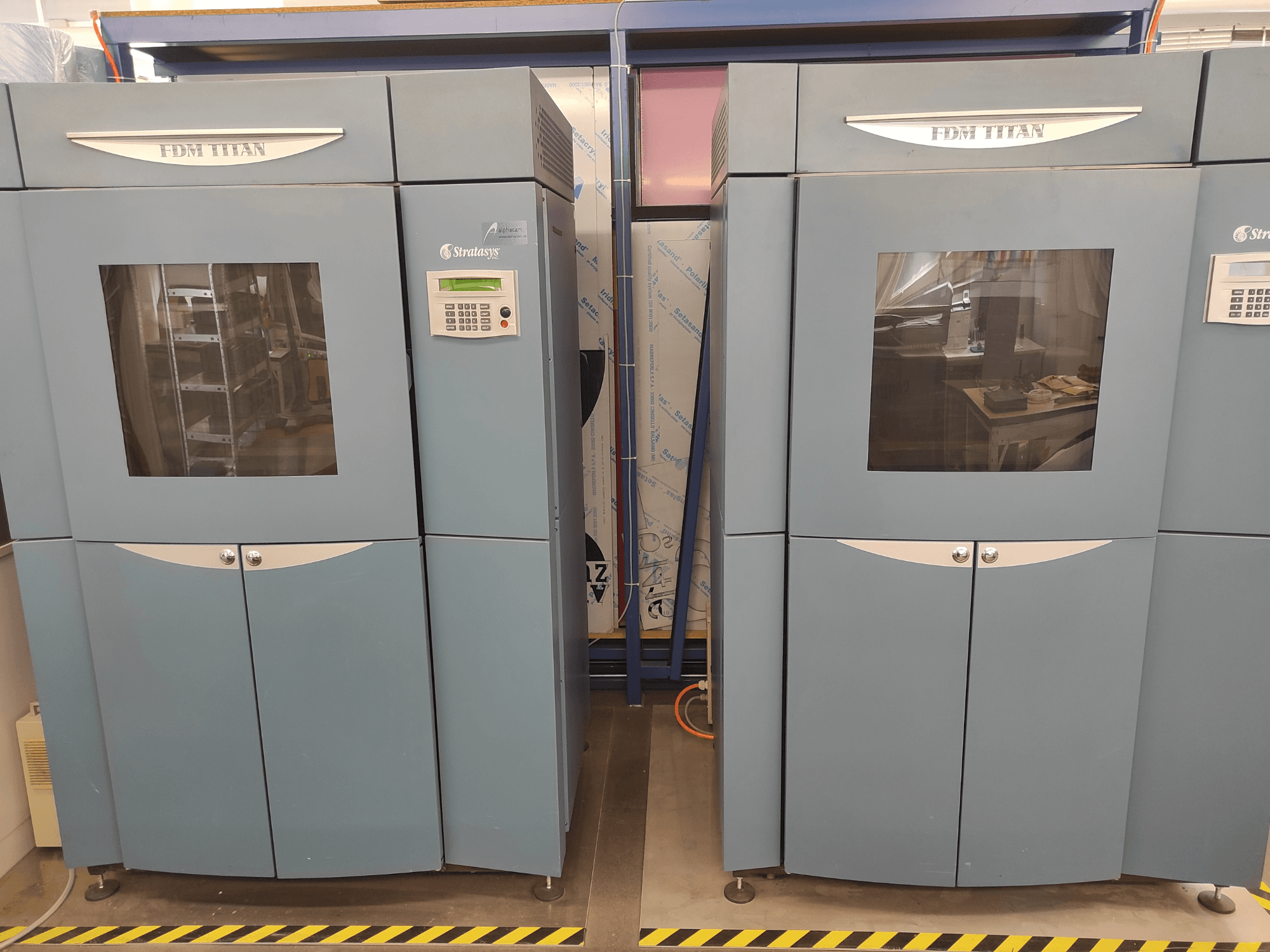 Drukarka 3D FDM TitanTI firmy Stratasys, widok z przodu, z podwójnymi drzwiczkami i panelem sterowania, umieszczona w środowisku przemysłowym.