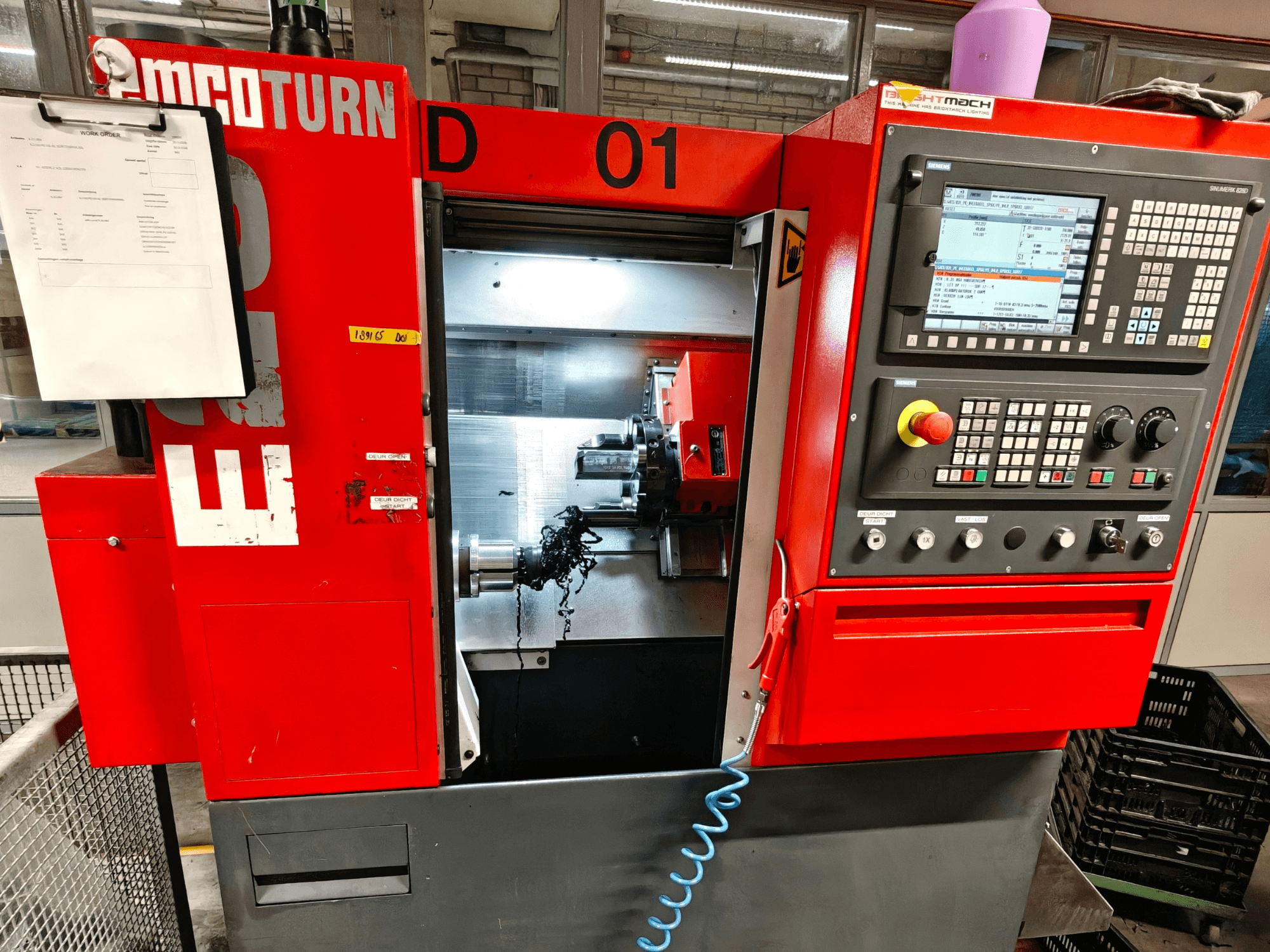 Widok z przodu tokarki poziomej EMCO TURN E25 z elementami sterującymi, uchwytem narzędziowym i obszarem roboczym z wiórami.