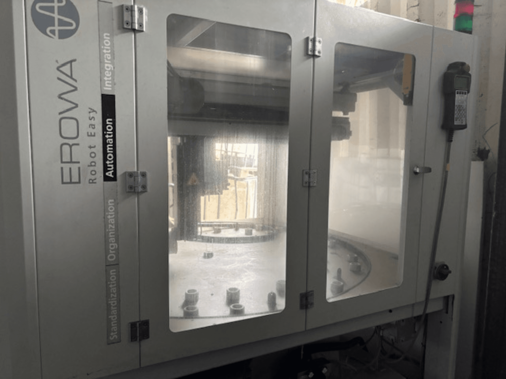 Widok z przodu EROWA Robot Easy Automation; przezroczyste drzwi, widoczne elementy automatyki i panel sterowania.