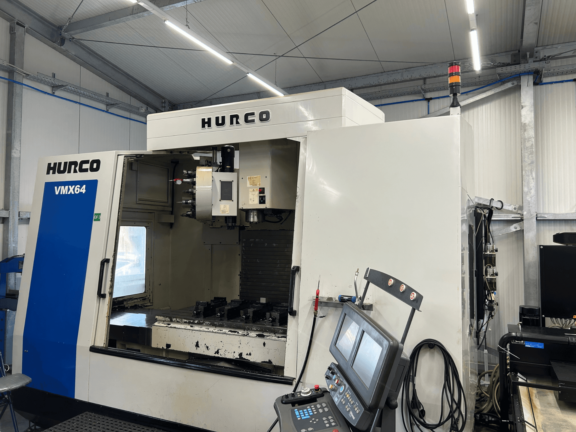 Pionowe centrum obróbcze Hurco VMX 64, widok z przodu, przedstawiający panel sterowania oraz otwartą przestrzeń roboczą z narzędziami.