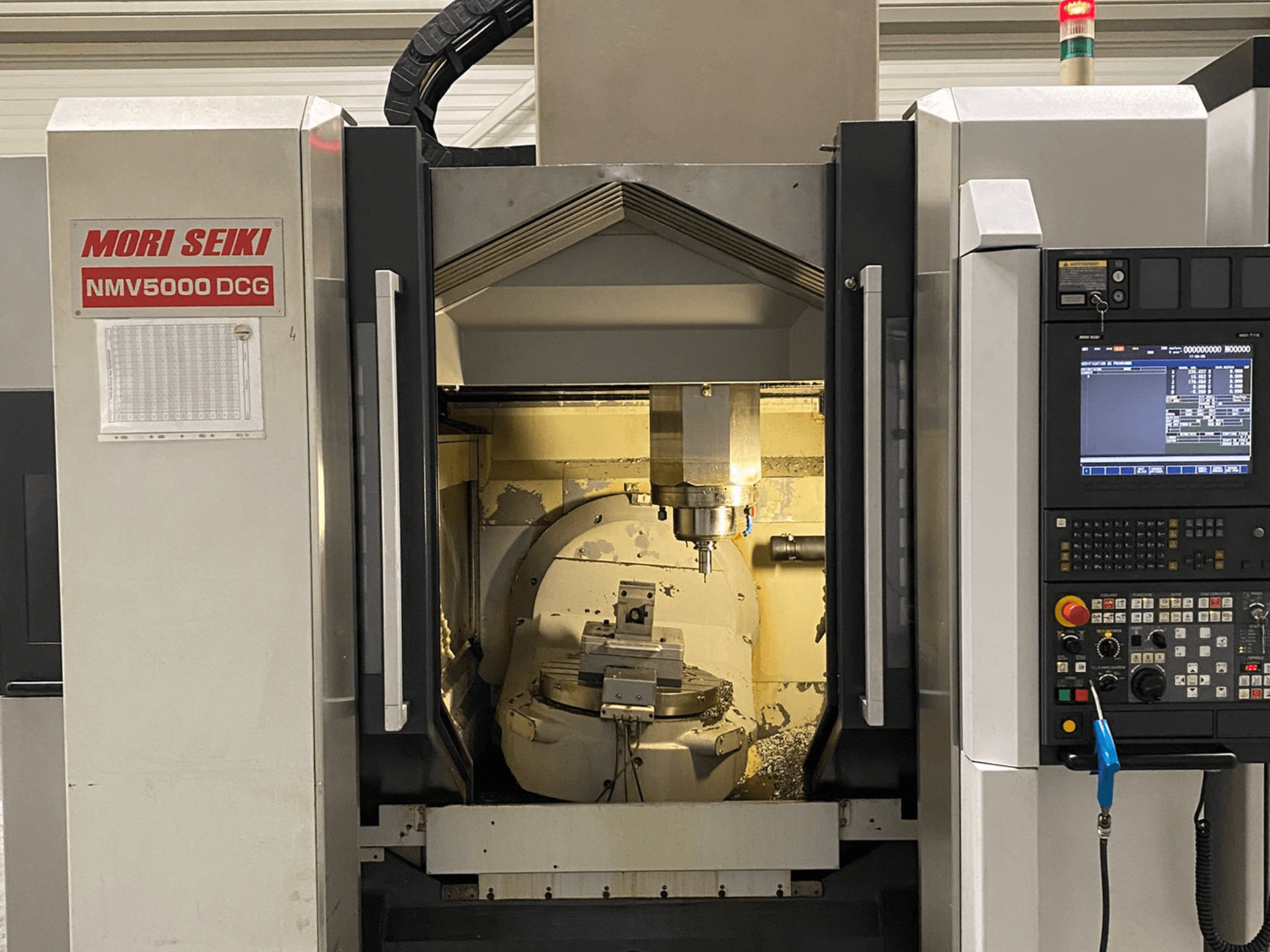 Uniwersalne centrum obróbcze MORI SEIKI NMV 5000DCG, widok z przodu przedstawiający panel sterowania i wewnętrzny obszar obróbki.