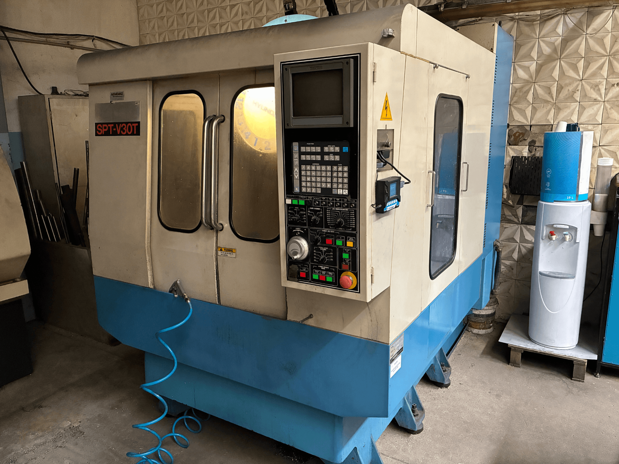 Maszyna CNC SPT-V30T w kolorze niebieskim i białym, widok z przodu pokazujący panel sterowania, drzwi i wąż powietrza. Idealna do precyzyjnej obróbki.
