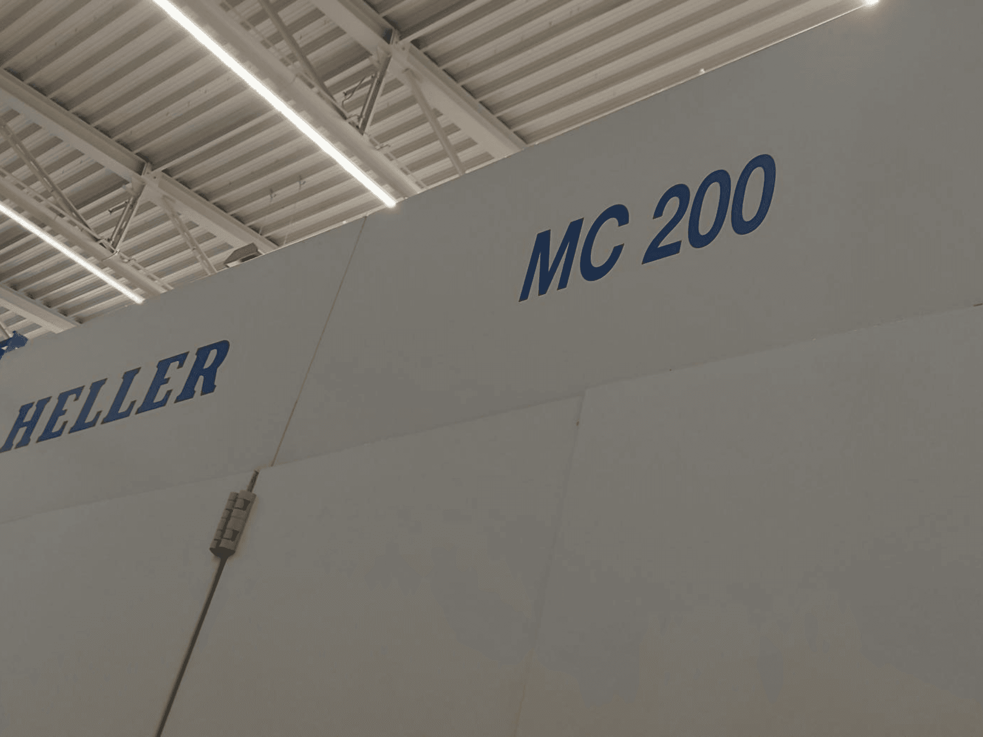 Poziome centrum obróbcze Heller MC 200, pokazane z boku, z niebieskim napisem marki i modelu na białej powierzchni.
