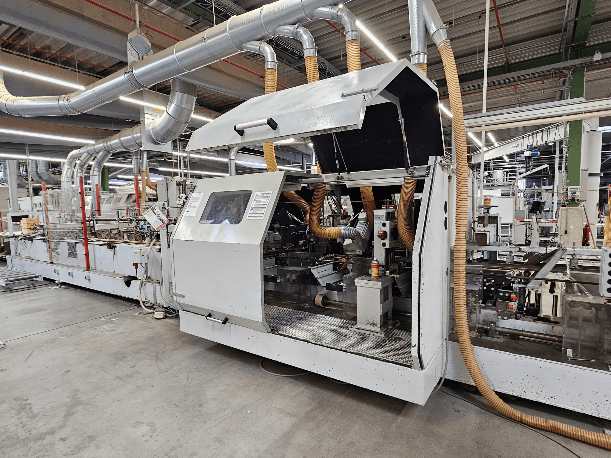 Okleiniarka HOMAG FG63 w ustawieniu fabrycznym, widok z boku pokazujący komponenty operacyjne i system odsysania pyłu.