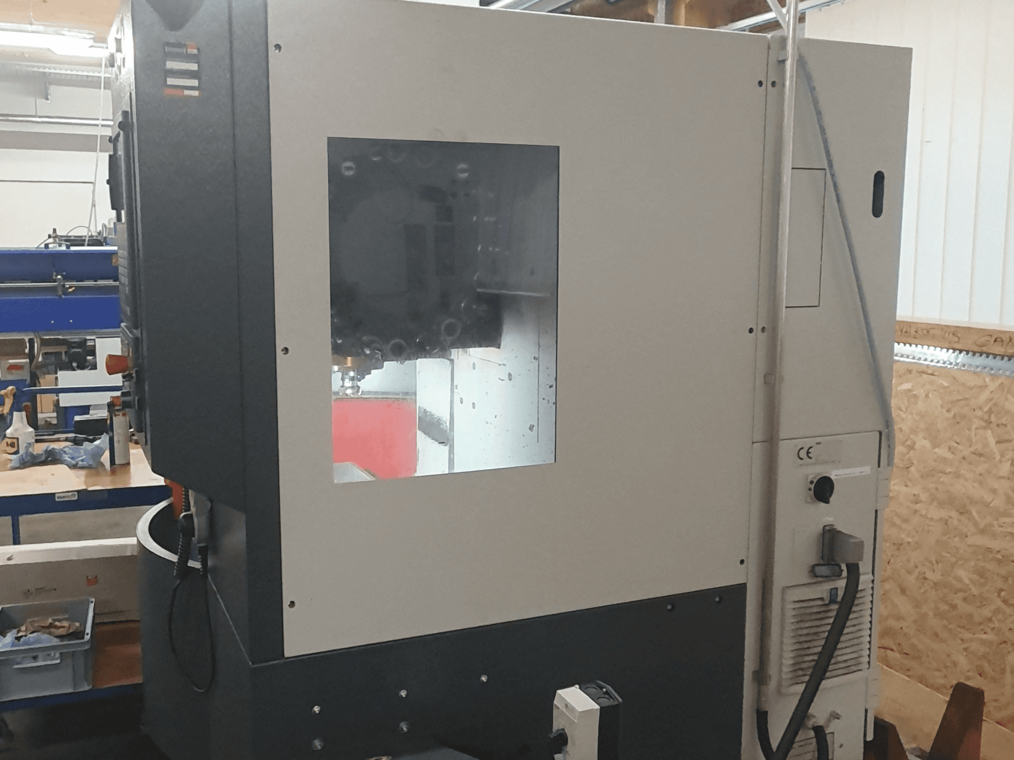 Widok z boku maszyny do obróbki metalu z widocznym panelem sterowania, dużym oknem podglądu i skomplikowanymi elementami wewnętrznymi.