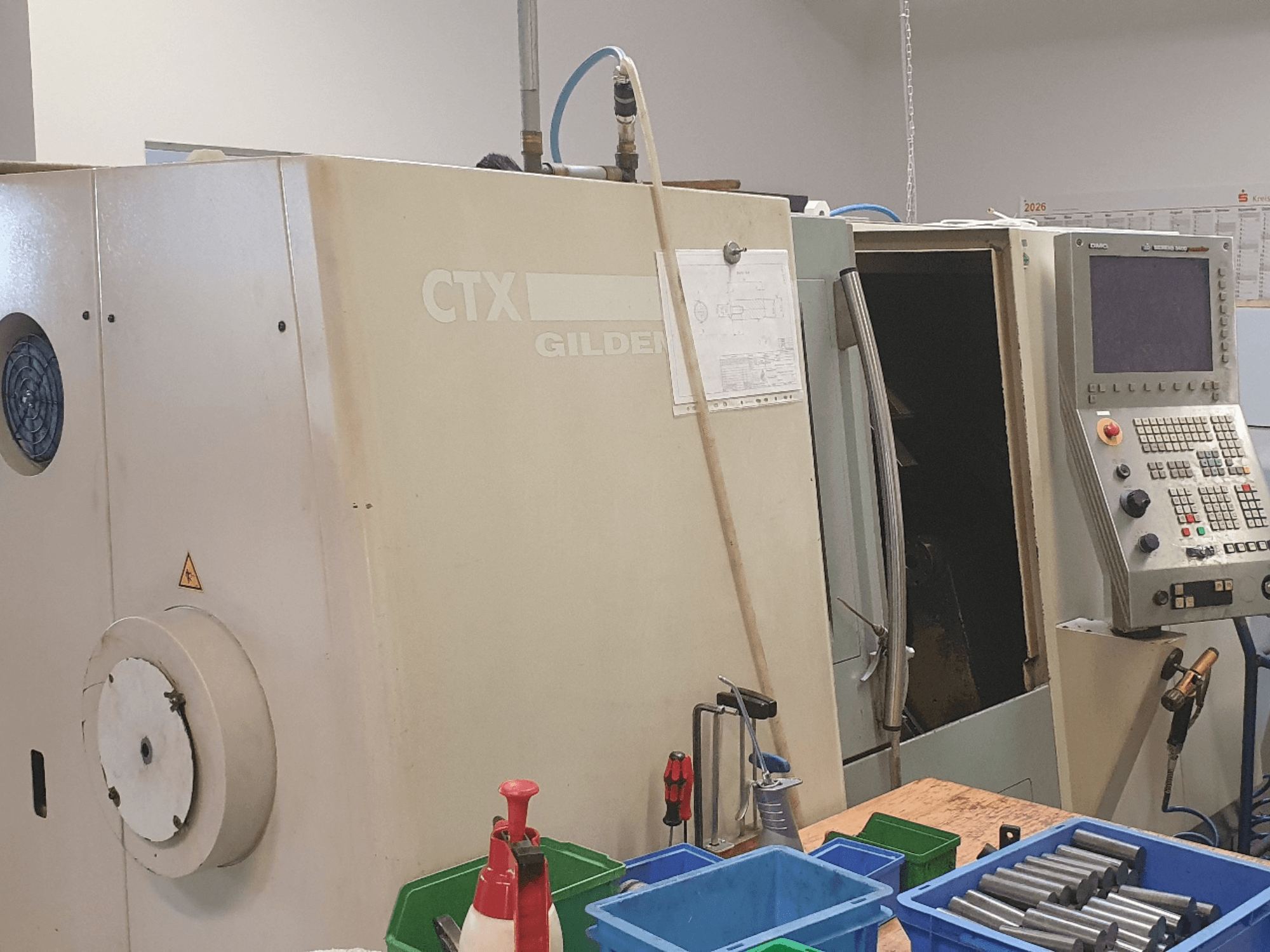 Widok z przodu poziomej tokarki DMG GILDEMEISTER CTX 310, widoczny panel sterowania, na pierwszym planie narzędzia i pojemniki.