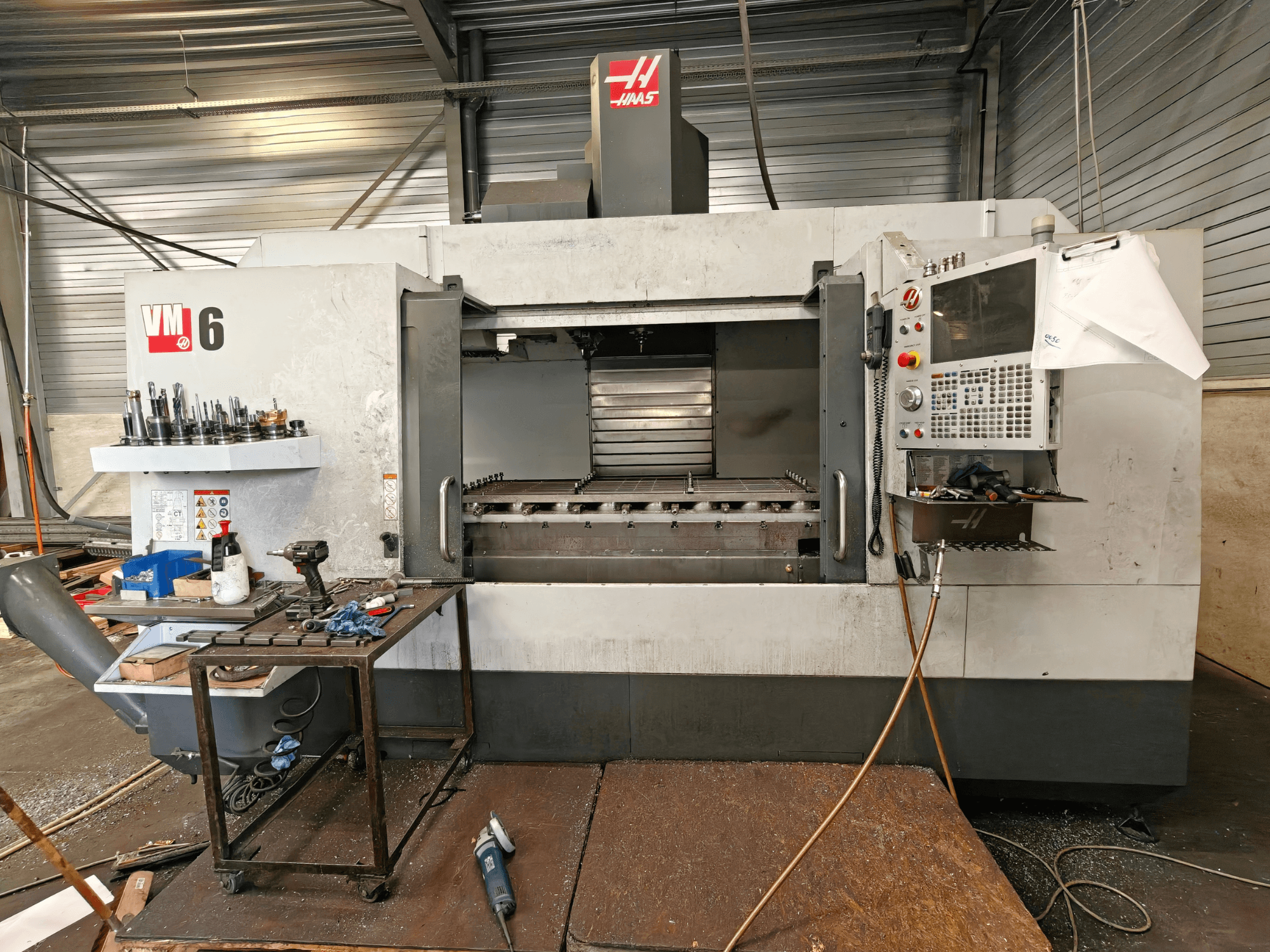 Pionowe centrum obróbcze Haas VM-6, widok z przodu, z widocznym magazynem narzędzi, panelem sterowania oraz zanieczyszczeniami w obszarze roboczym.