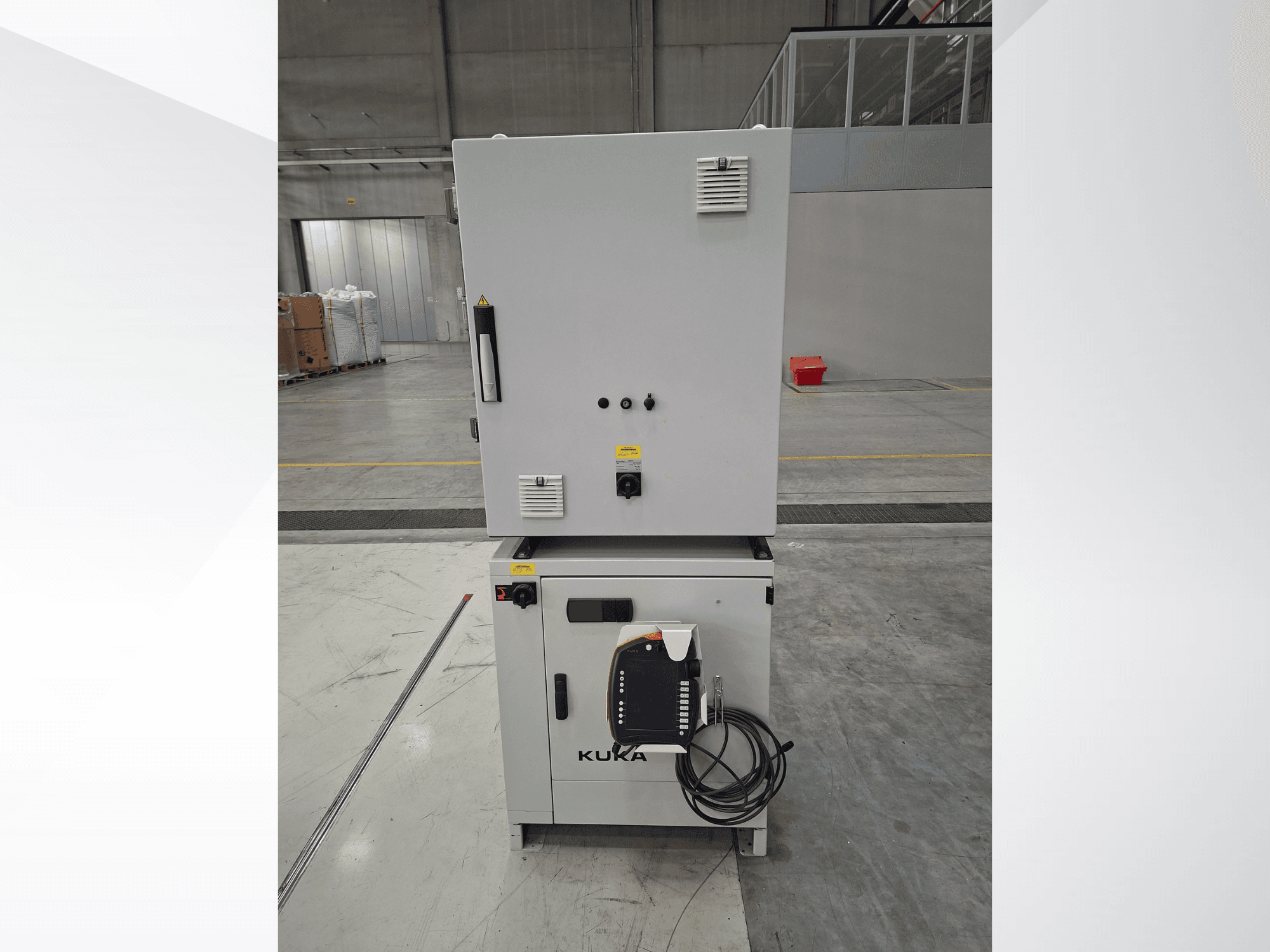 Sterownik ramienia robota KUKA KR 90 R2700 PRO C4 FLR – widok z przodu przedstawiający panel sterowania i etykiety bezpieczeństwa w przestronnym magazynie.