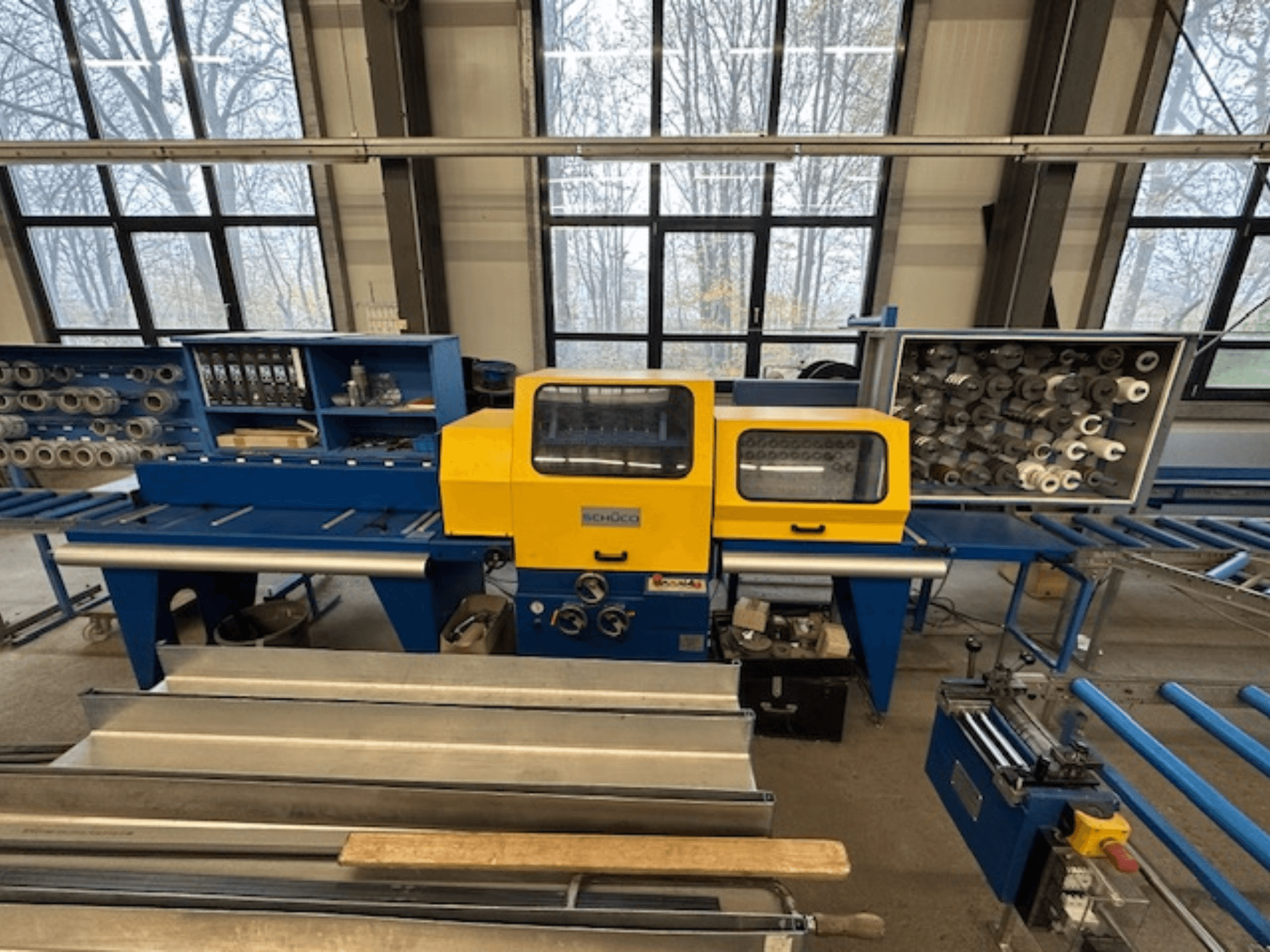 Widok z przodu obrabiarki SCHÜCO ISOMAT 4 z żółtym panelem sterowania, wieloma rolkami i schowkiem.