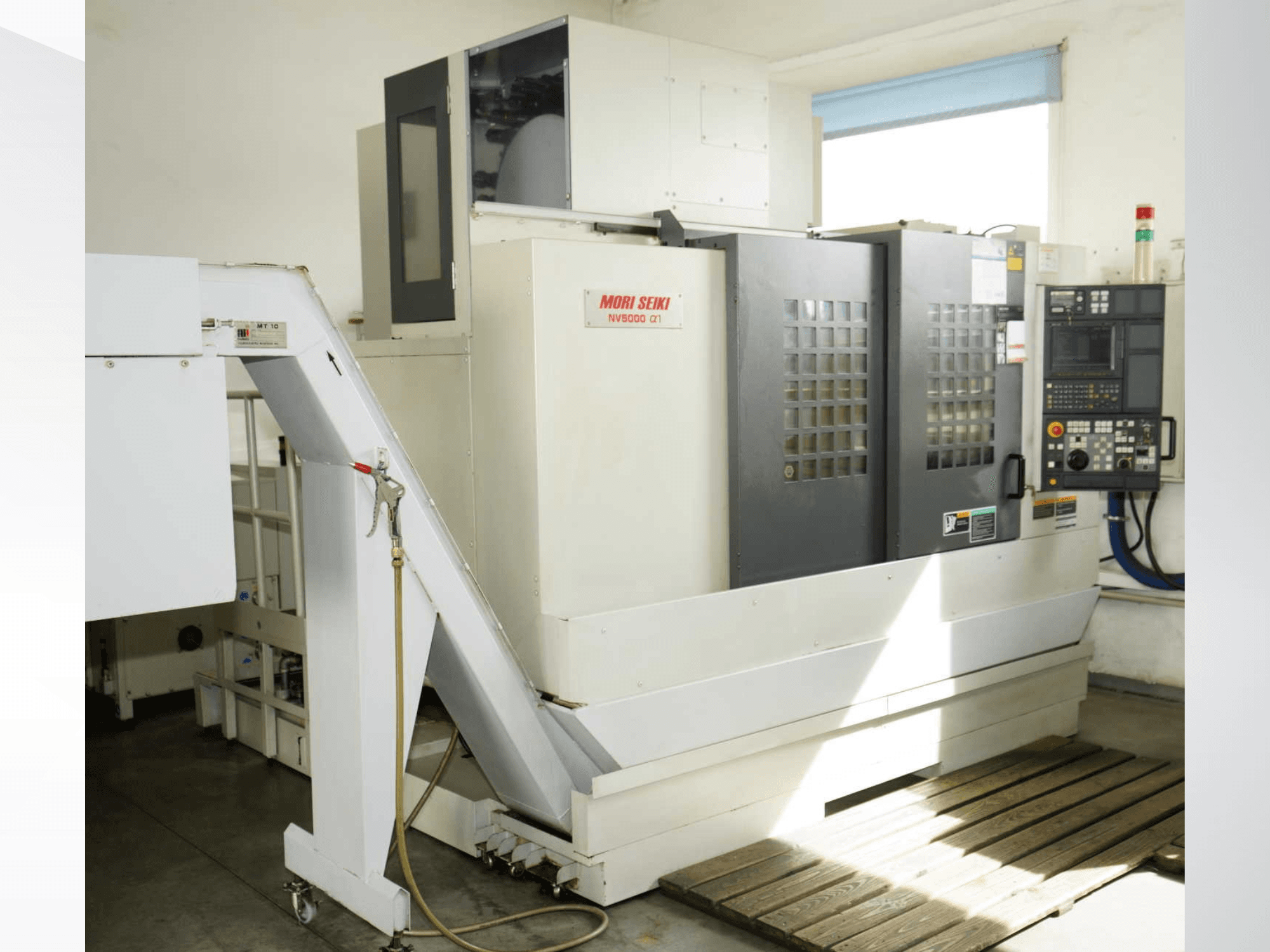 Pionowe centrum obróbcze MORI SEIKI NV 5000 alpha1 widziane z przodu, przedstawiające panel sterowania, elementy zabezpieczające oraz obszar załadunku.