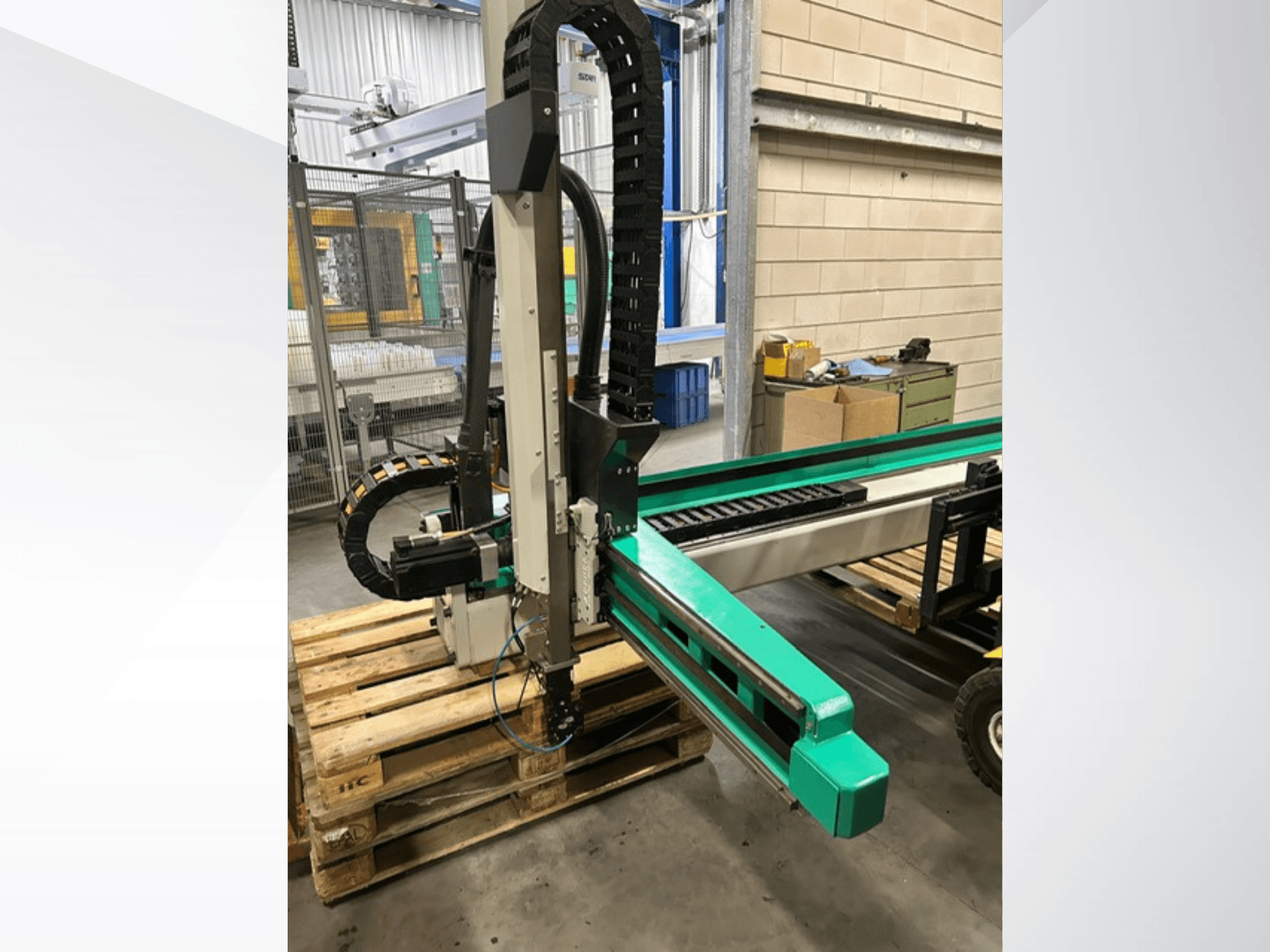 Arburg Multilift Select 15kg quer, widok z boku systemu przenoszenia detali na drewnianych paletach, pokazujący ramię robota i komponenty sterujące.