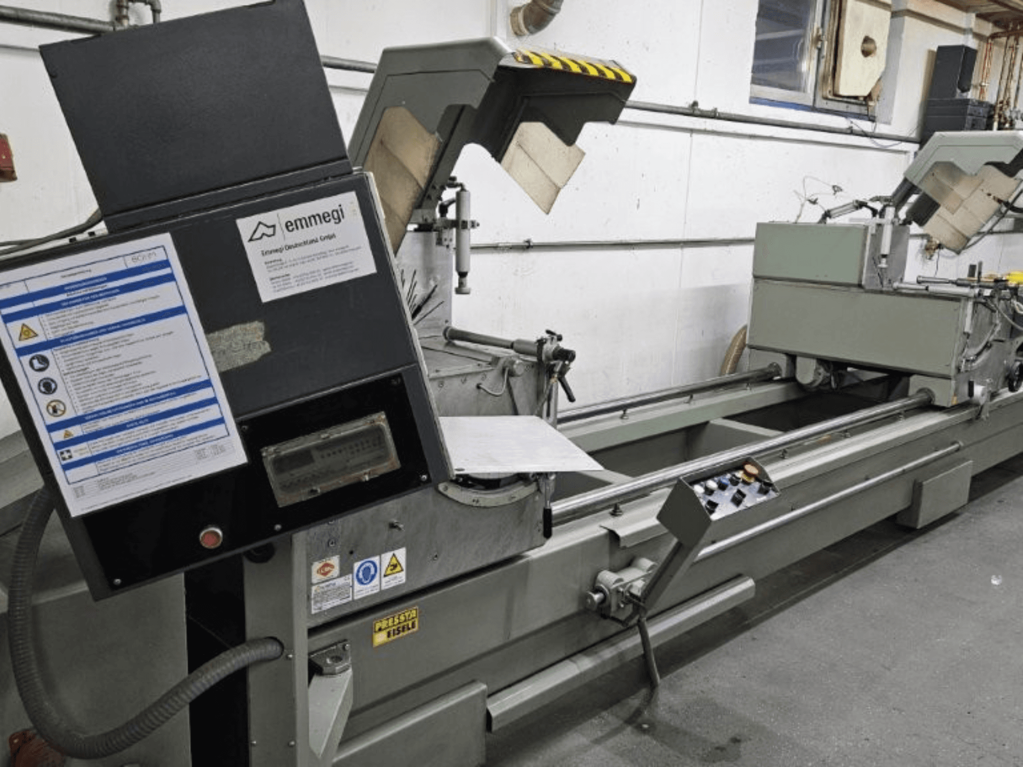 Przemysłowa przecinarka Emmegi, widok z przodu, z panelem sterowania, etykietami bezpieczeństwa i elementami operacyjnymi.