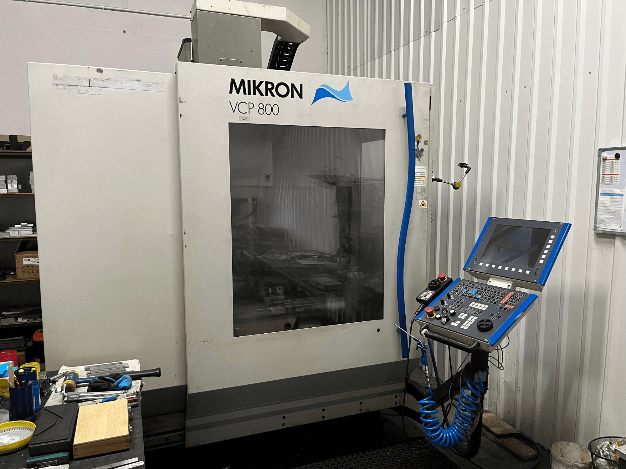 Pionowe centrum obróbcze MIKRON VCP 800, widok z przodu, z panelem sterowania i narzędziami na stole roboczym na pierwszym planie.