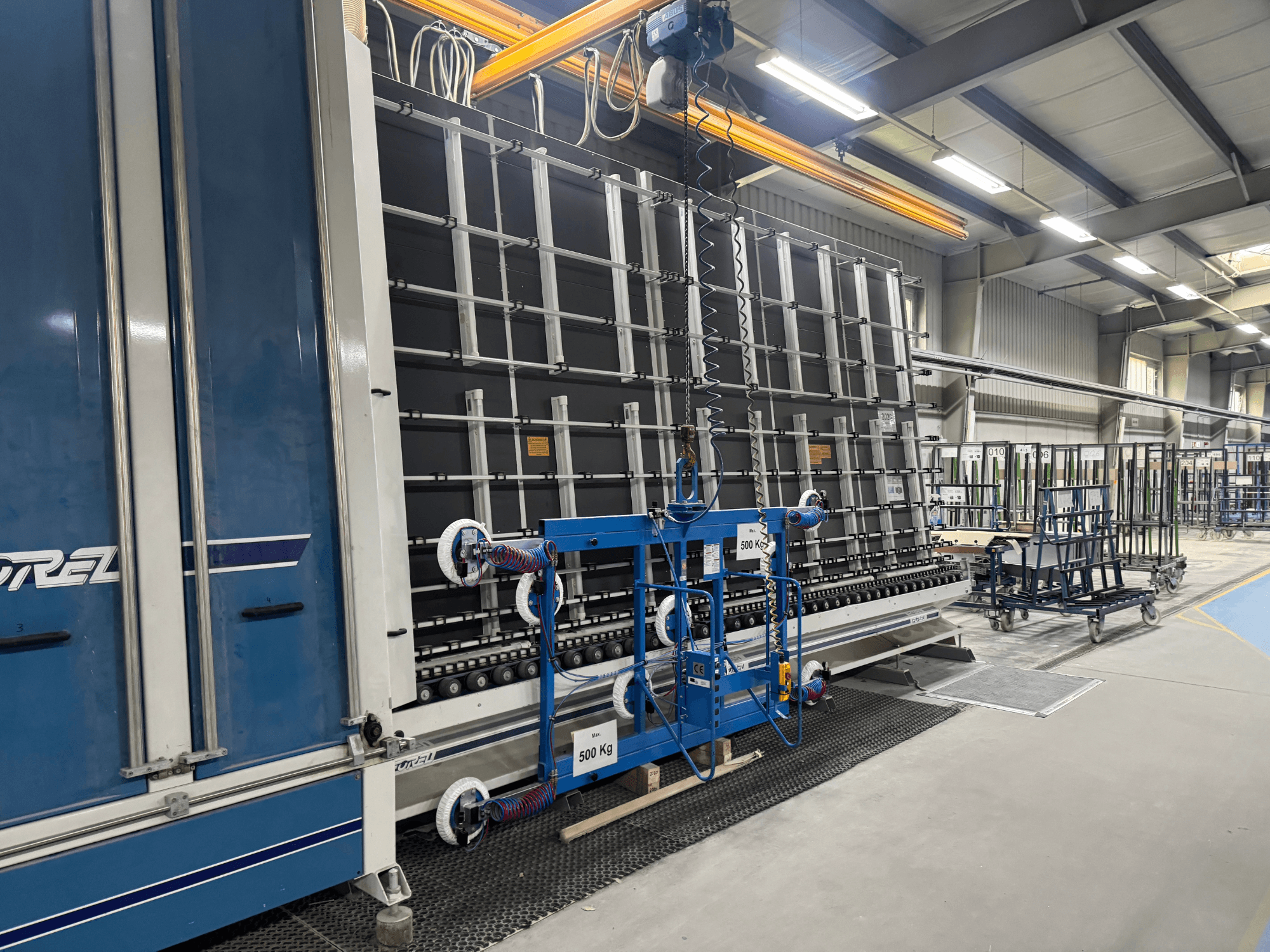 Sprzęt przemysłowy firmy Drel z dużą ramą i mechanizmem podnoszącym, pokazany z boku w warunkach fabrycznych.