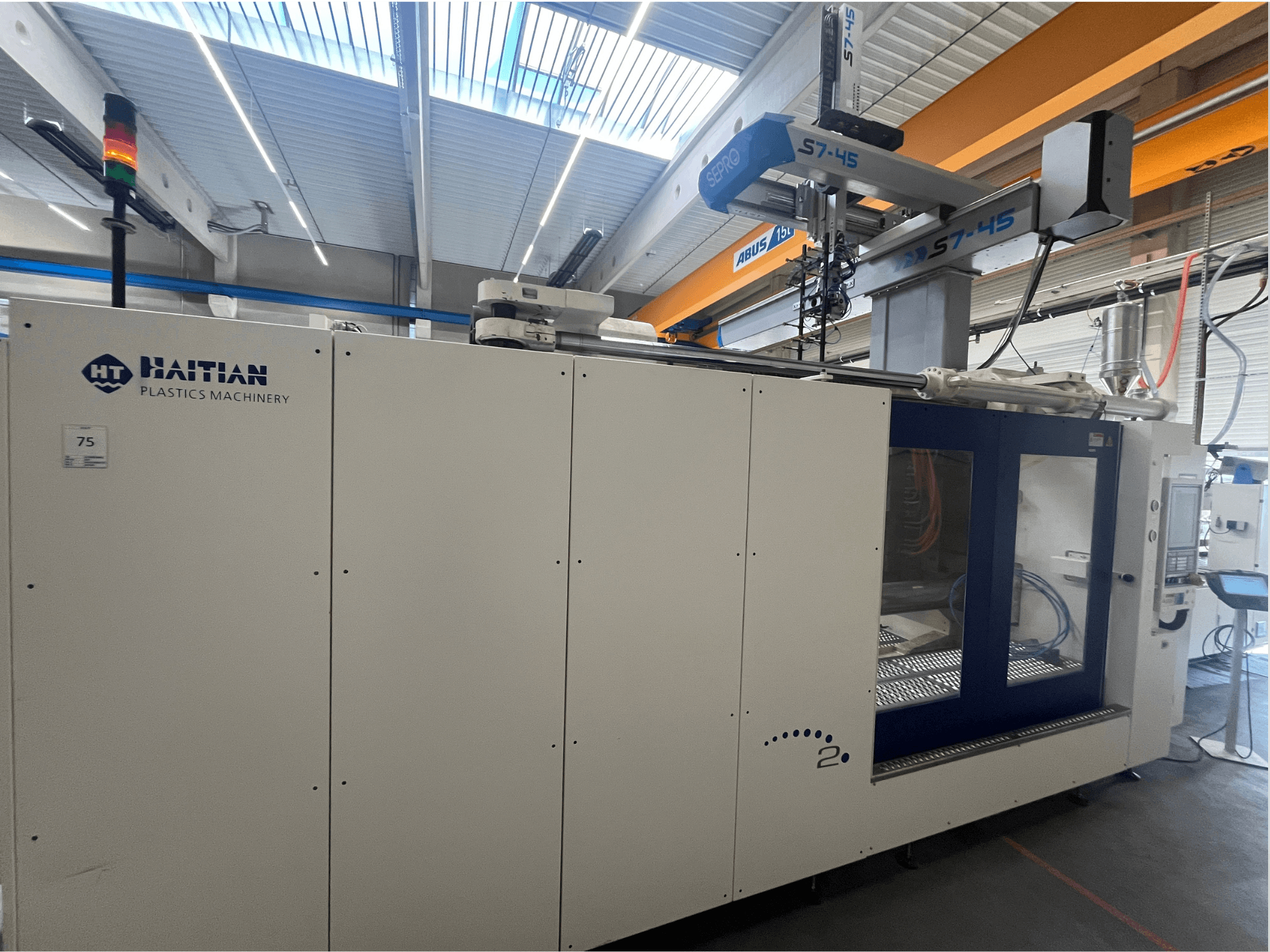 Haitańska wtryskarka S7-45 w widoku z boku z panelem sterowania i wskaźnikiem bezpieczeństwa. Biało-niebieski design.