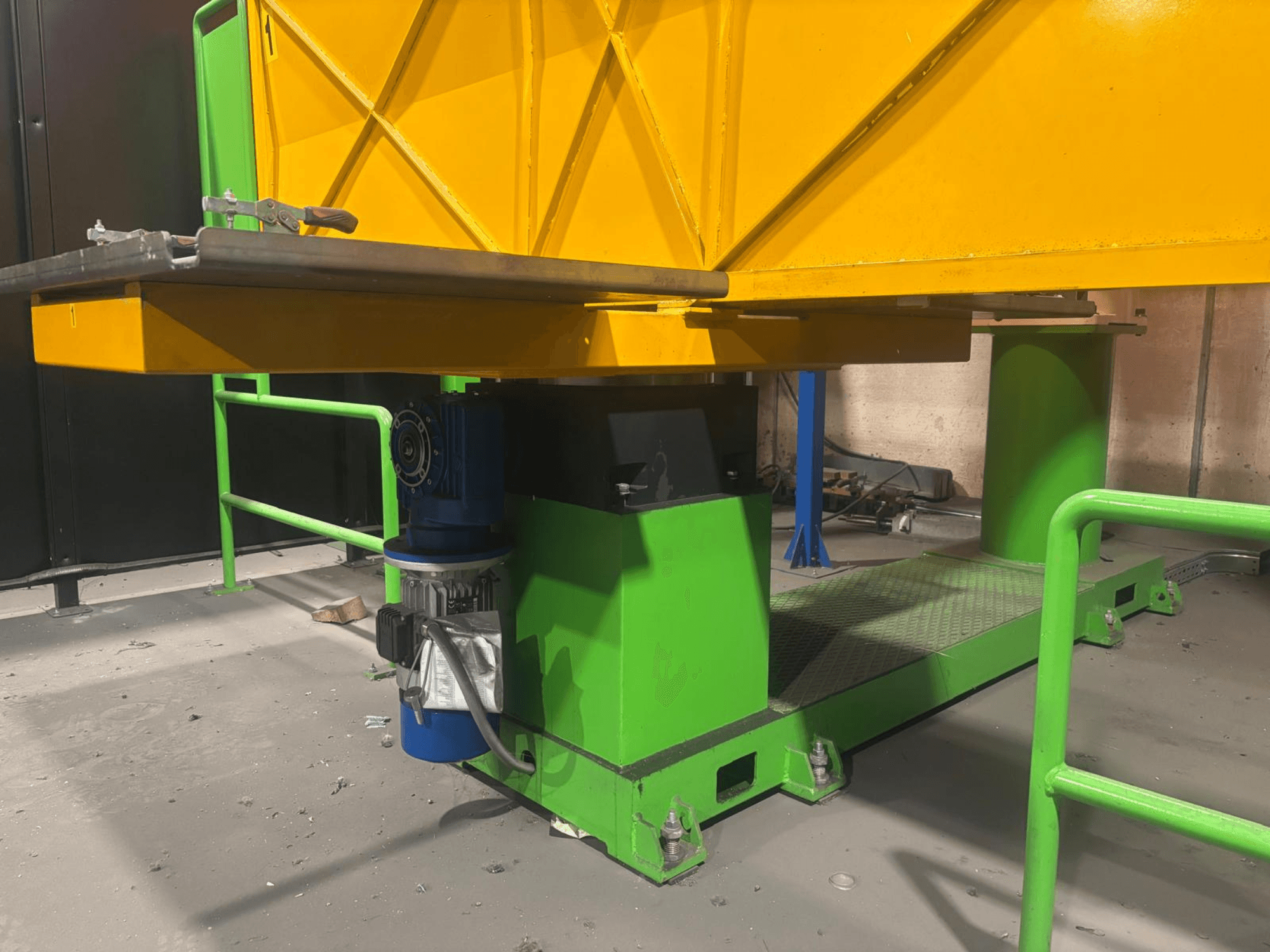 Zielono-żółta maszyna przemysłowa z niskiego widoku z przodu, z silnikiem i platformą o teksturowanej powierzchni.