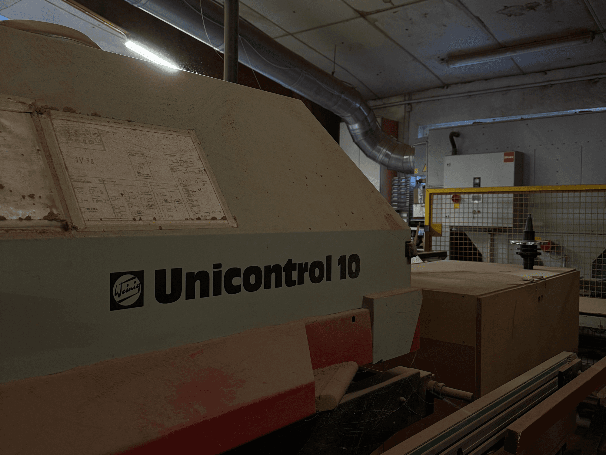 Maszyna Weinig Unicontrol 10 widziana z boku, zakurzona powierzchnia, schematy techniczne widoczne na przednim panelu.