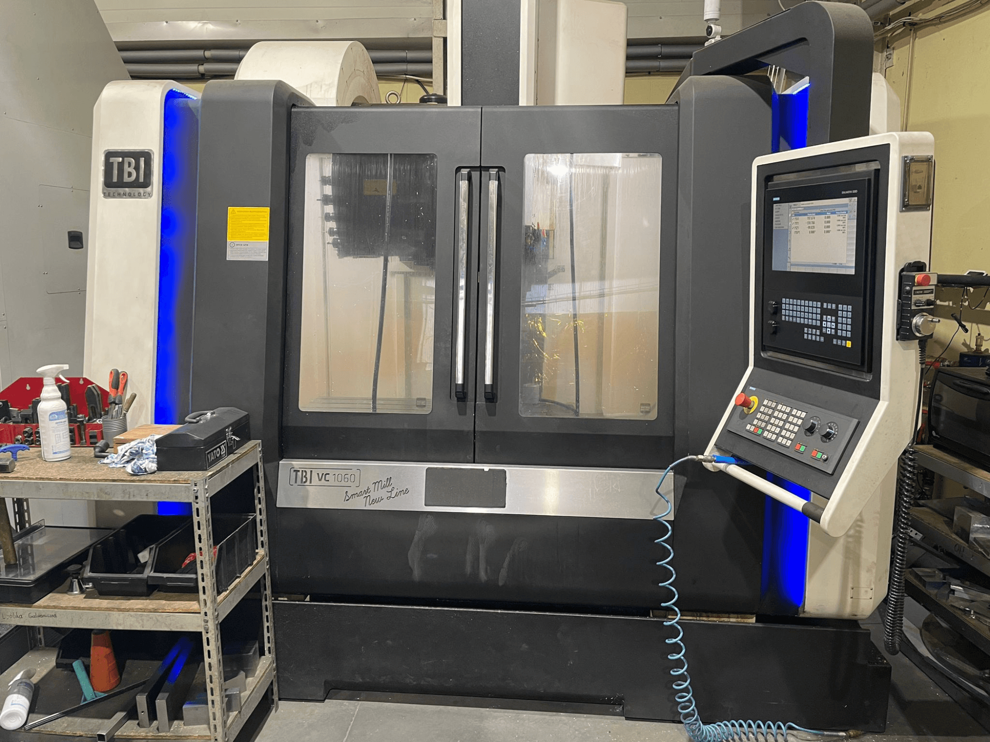 Pionowe centrum obróbcze TBI VC 1060 HH, widok z przodu, panel sterowania, osłona przeciwpyłowa i podświetlane niebieskie akcenty.