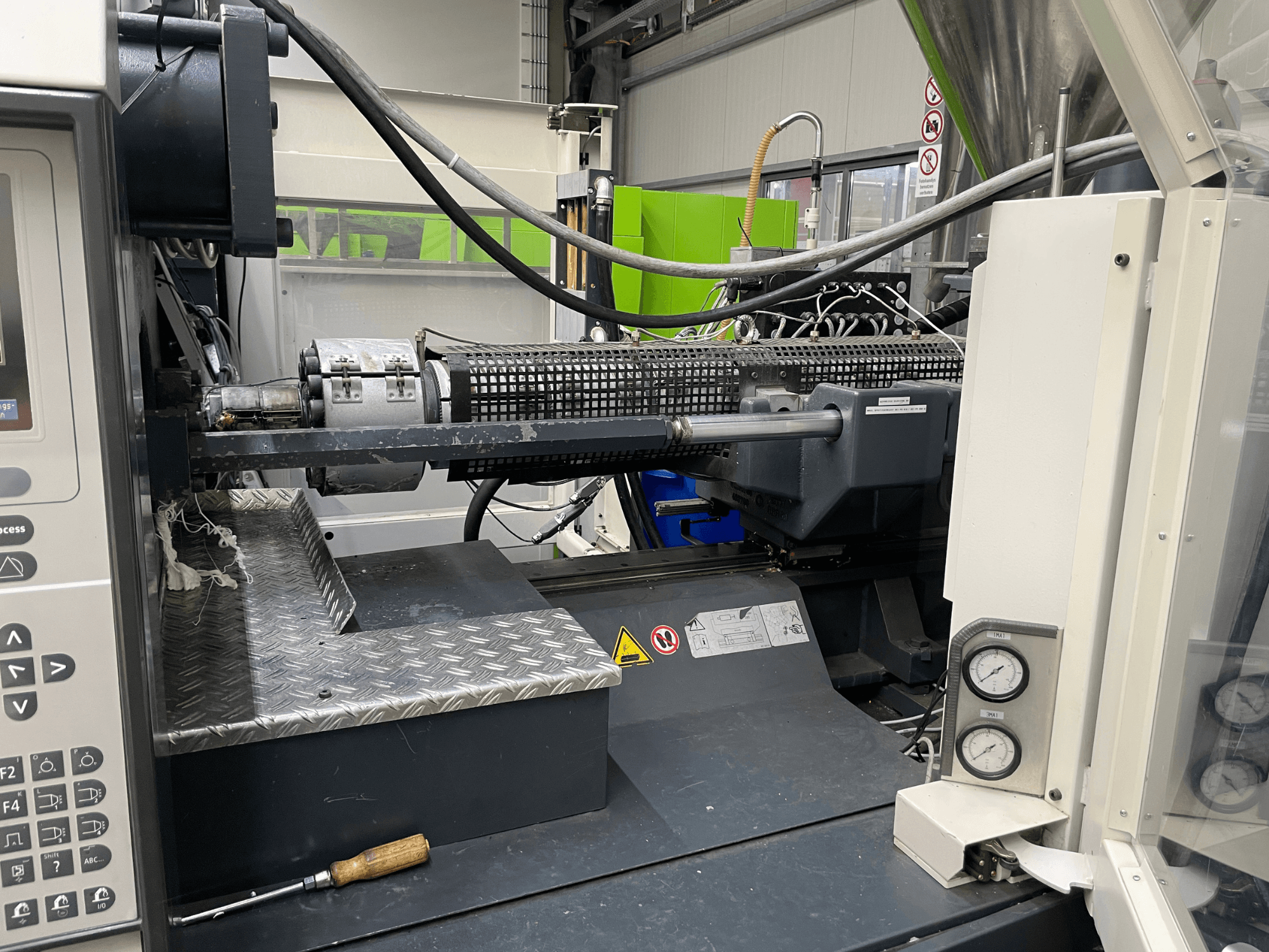 Widok z boku wtryskarki z widocznym panelem sterowania, wytłaczarką i manometrami, idealny do zadań produkcyjnych.