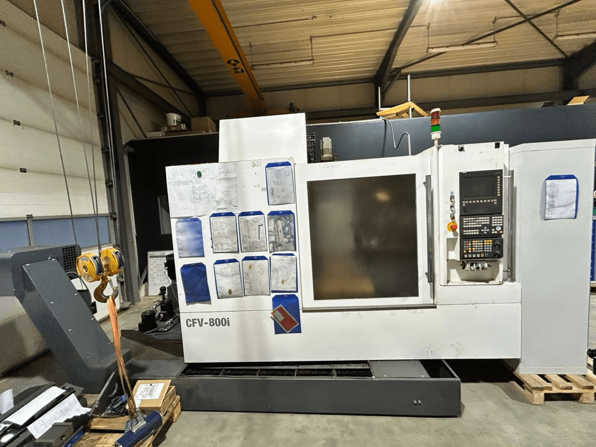Maszyna CNC CFV-800i pokazana w widoku z przodu, z panelem sterowania, dokumentami z boku i suwnicą w ustawieniu fabrycznym.