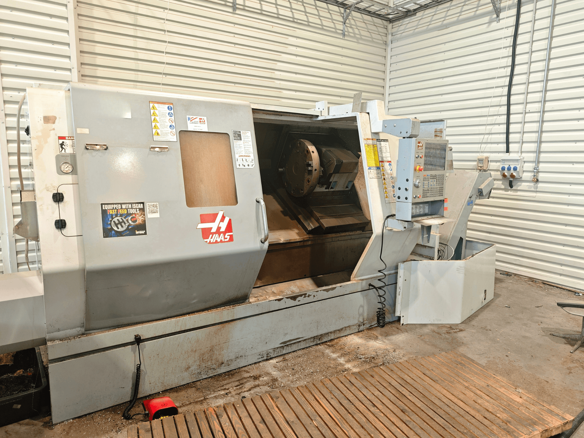 Pozioma tokarka Haas SL-40HE, widok z przodu, przedstawiająca panel sterowania, obszar roboczy oraz etykiety bezpieczeństwa.
