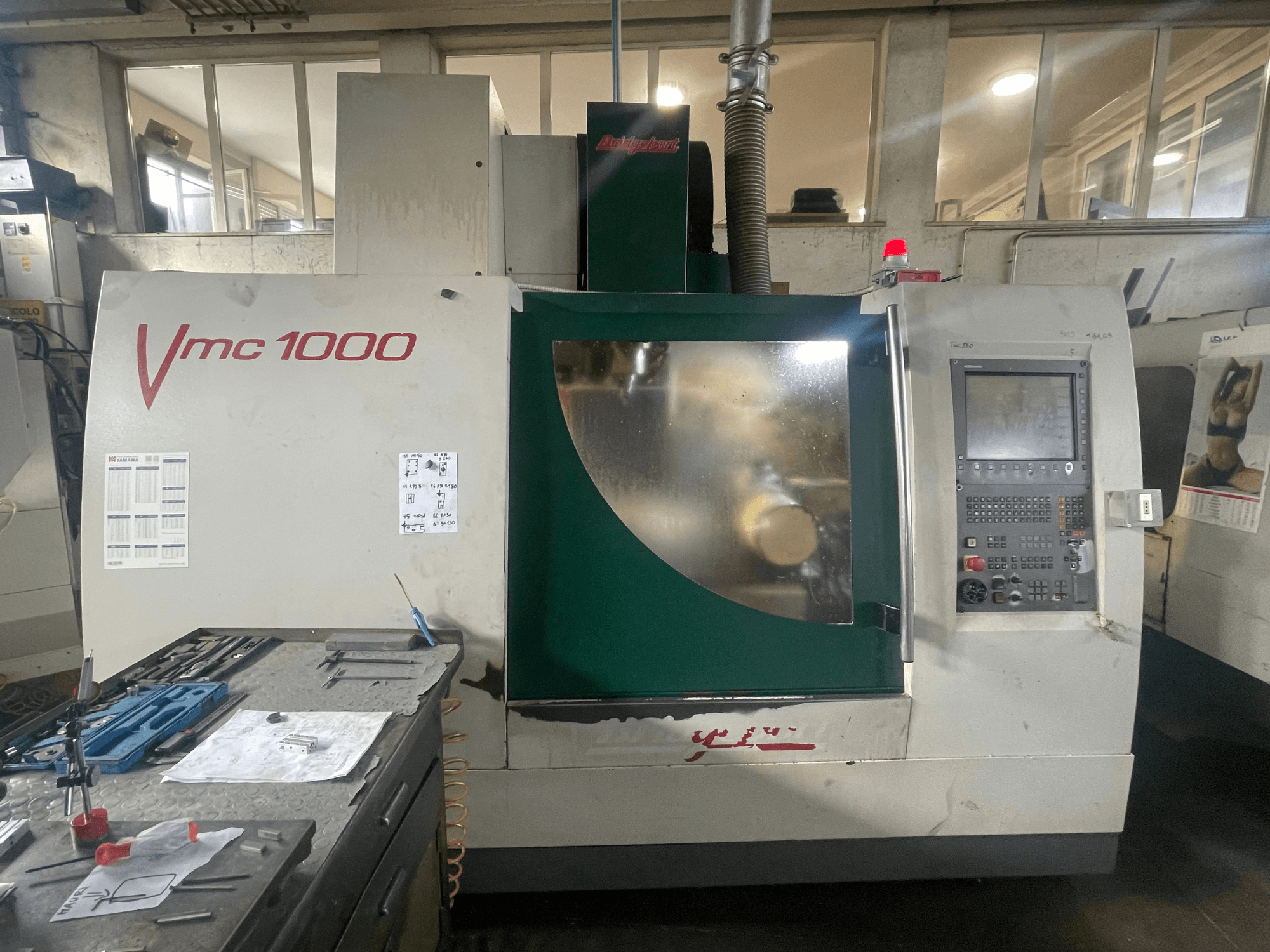 Pionowe centrum obróbcze Bridgeport VMC 1000/30, widok z przodu, przedstawiający panel sterowania i korpus głównego urządzenia, z narzędziami w pobliżu.