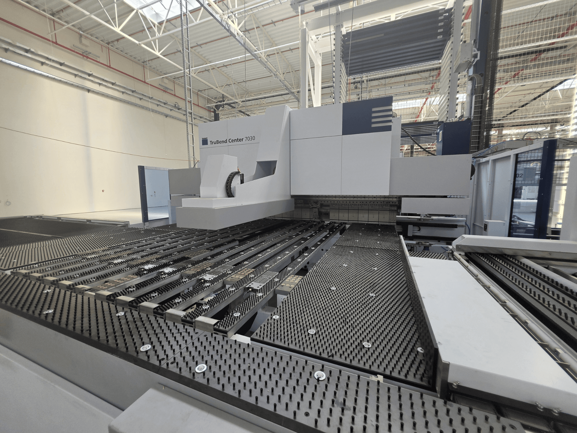 Giętarka TRUMPF TruBend Center 7030 w warunkach fabrycznych – widok z przodu przedstawiający skomplikowaną konstrukcję stołu roboczego i ramienia giętącego.